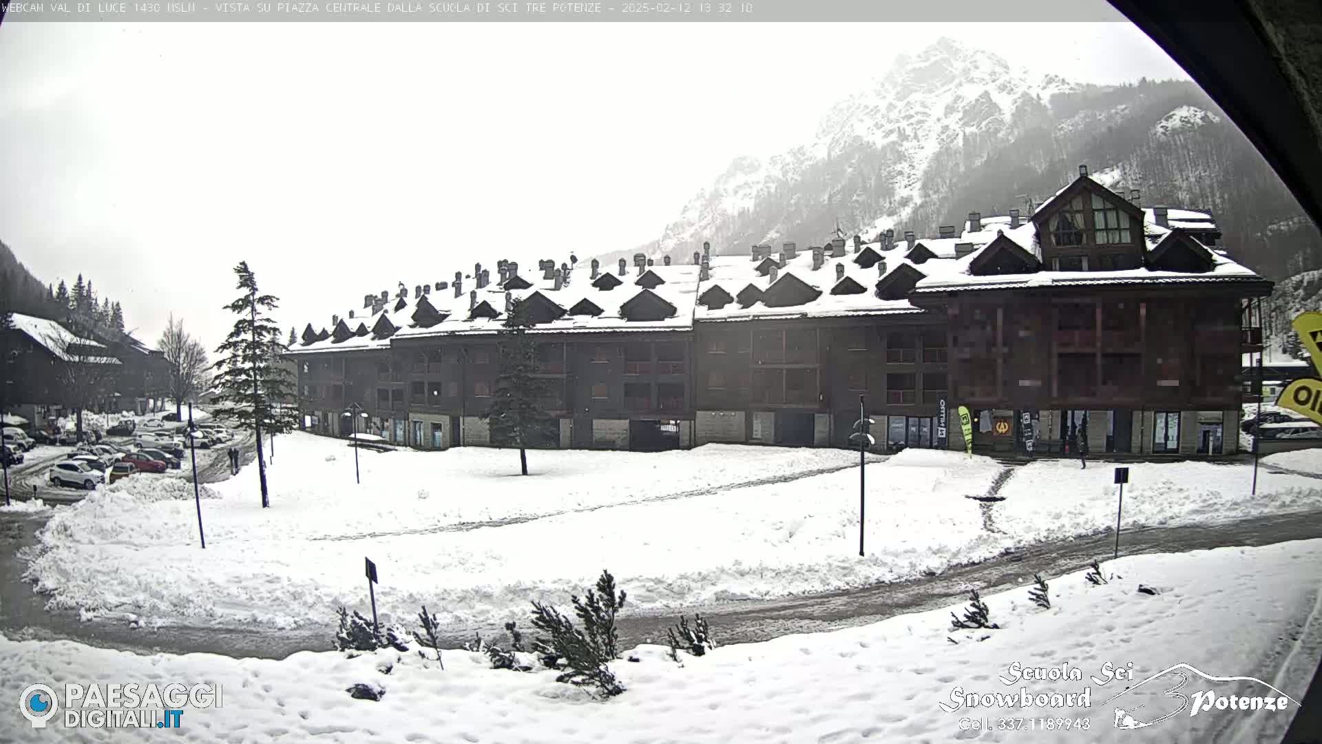 A snow-covered plaza with a large, multi-unit building and a mountain in the background under overcast skies.