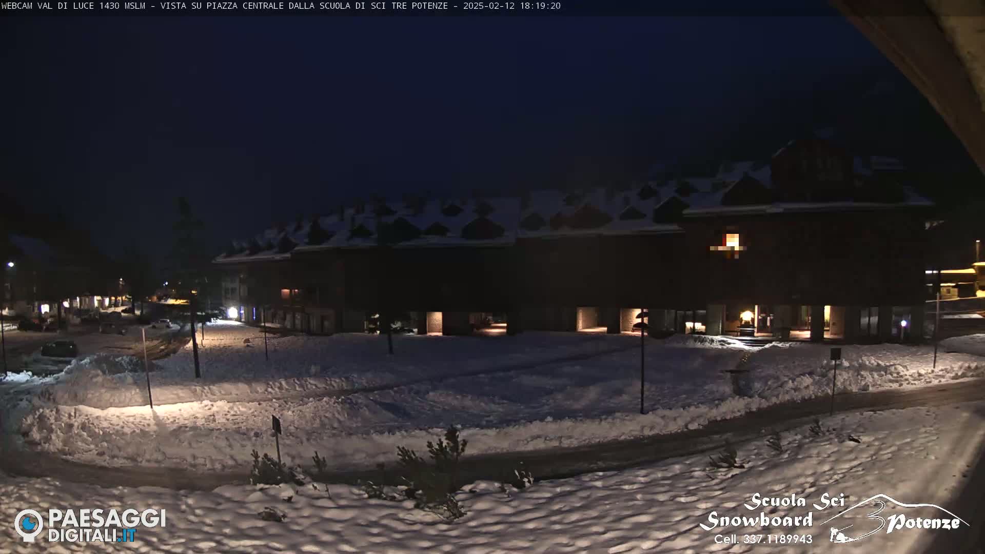 A snow-covered plaza at night, illuminated by lights from nearby buildings.