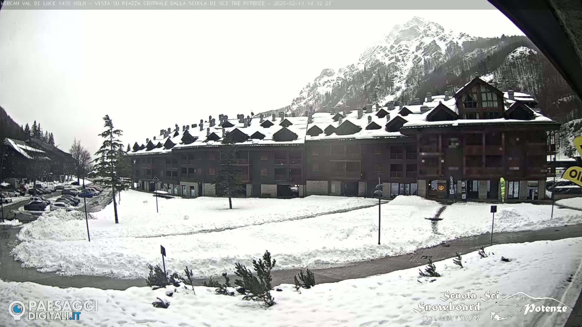 A snow-covered plaza sits in front of a multi-story building, with a mountain in the background under an overcast sky.