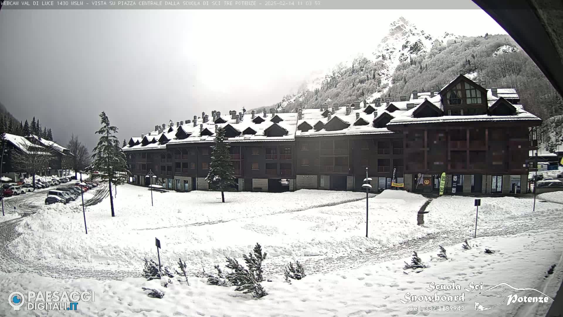 A snow-covered plaza in front of a multi-story building in a mountainous region under an overcast sky.