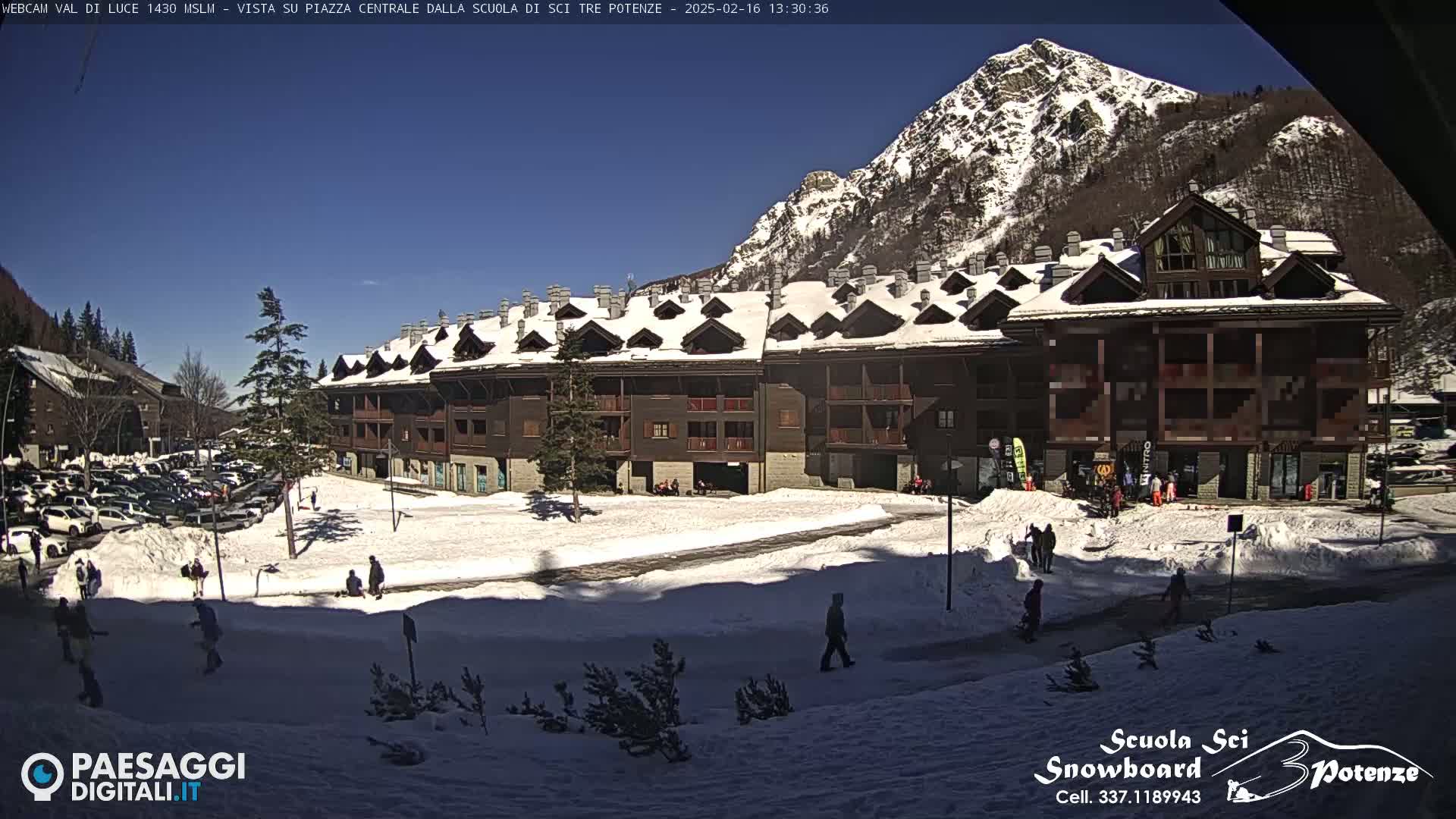 A snow-covered plaza with a large brown building and a mountain in the background under a clear blue sky.