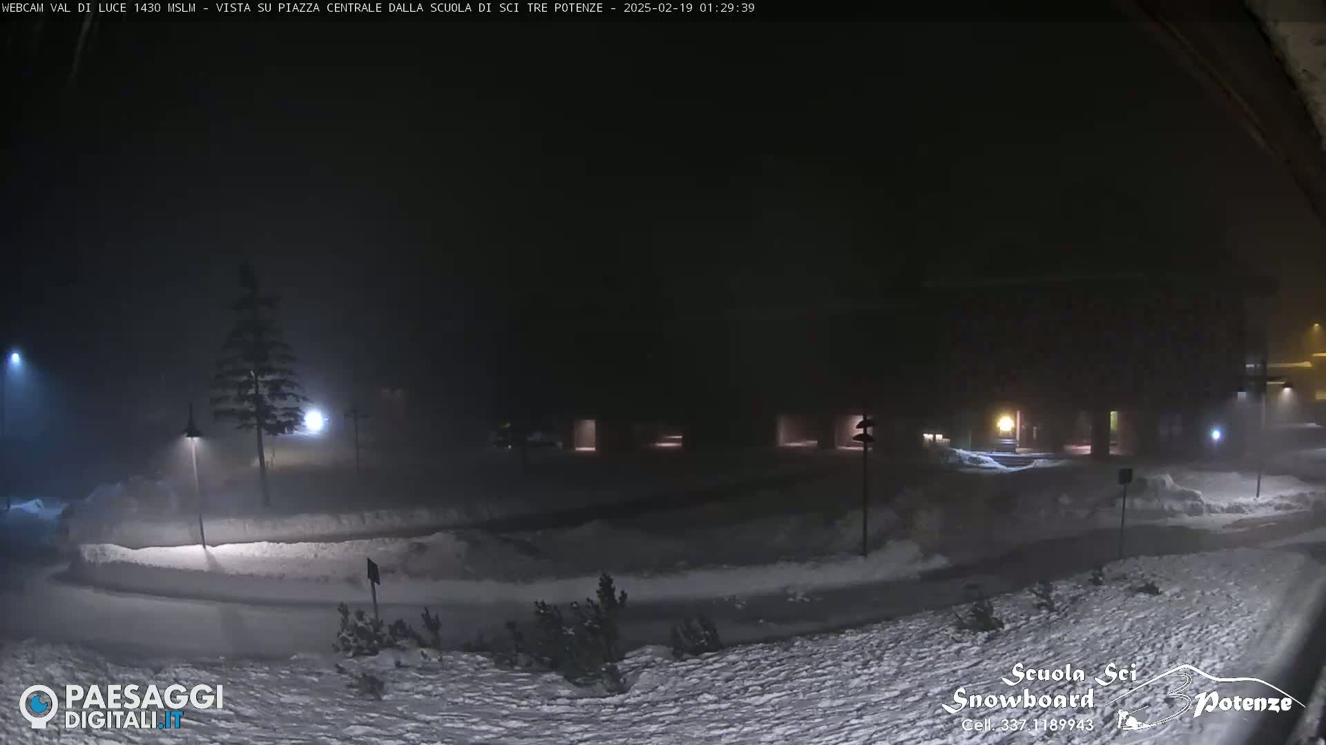 A snow-covered plaza is dimly lit at night under foggy conditions.