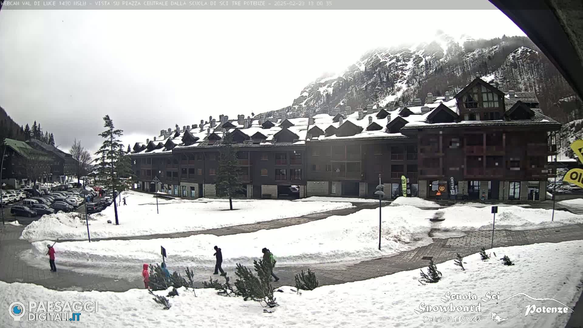 A snow-covered plaza in front of a multi-story building, with mountains in the background under an overcast sky.