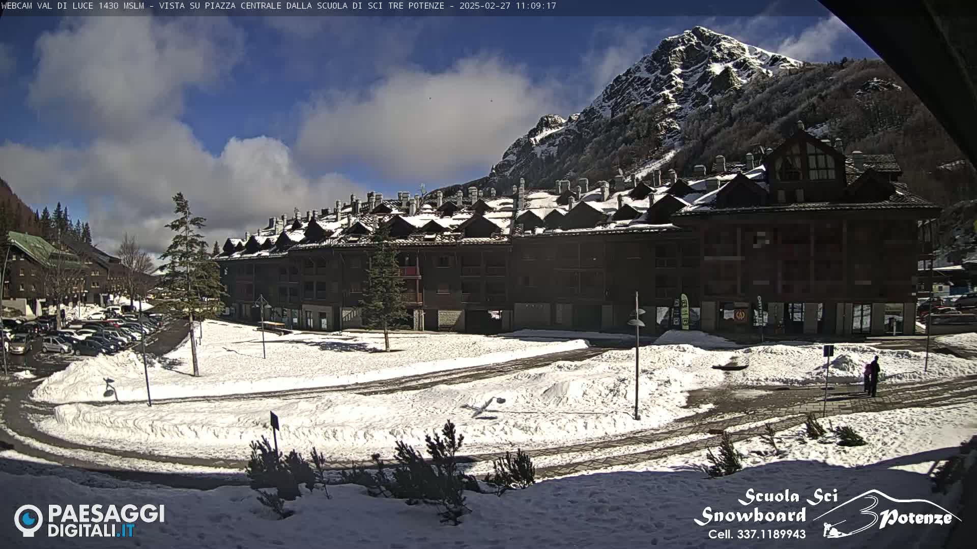 A snow-covered plaza with a multi-story building and a mountain in the background under a partly cloudy sky.