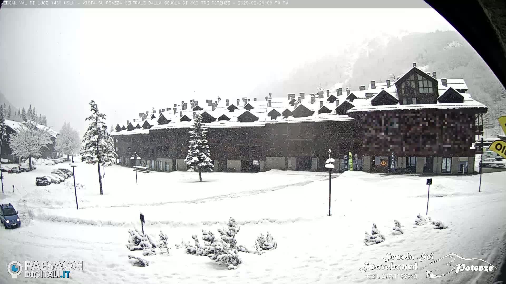 A snow-covered plaza with a large multi-story building in the background during a snowfall.