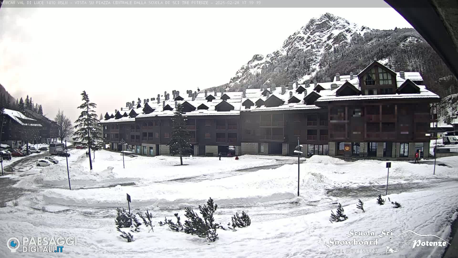 A snow-covered plaza sits in front of a large apartment building, with a mountain in the background under an overcast sky.