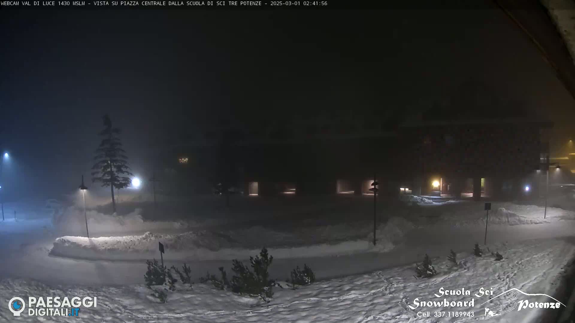 A snow-covered plaza at night is dimly lit by streetlights in foggy conditions.
