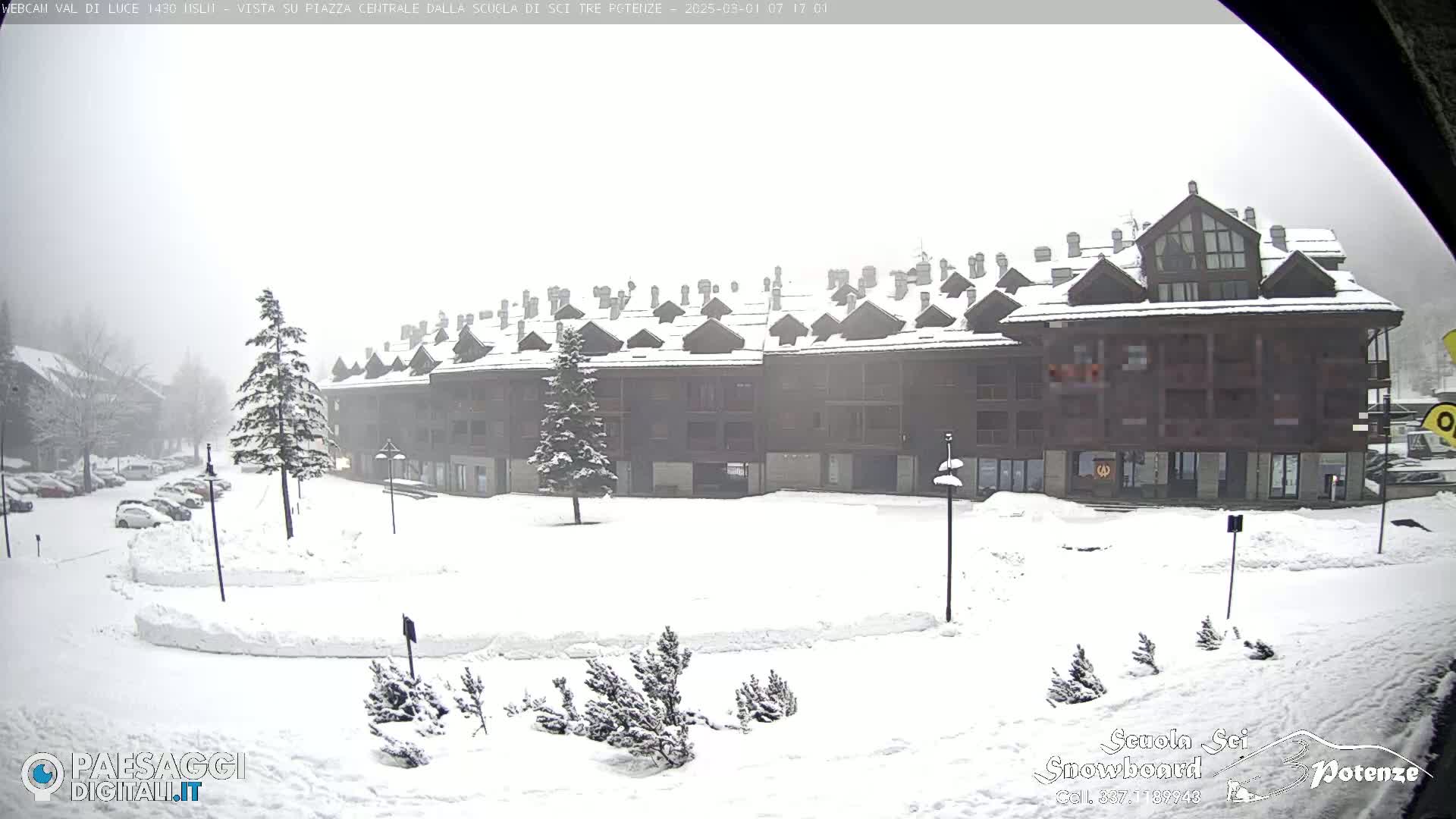 A snow-covered plaza sits in front of a long, multi-story building under a heavy, overcast sky.