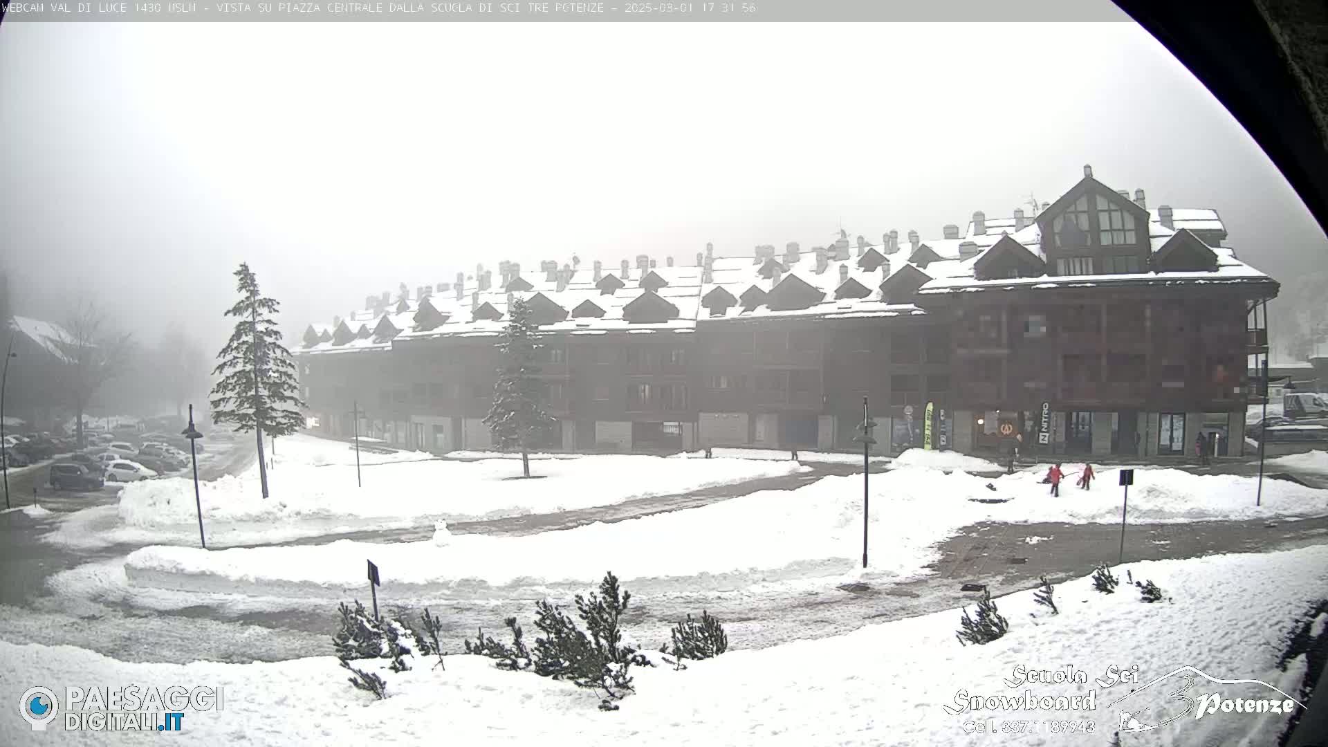 A snow-covered plaza sits in front of a multi-story building in foggy conditions.