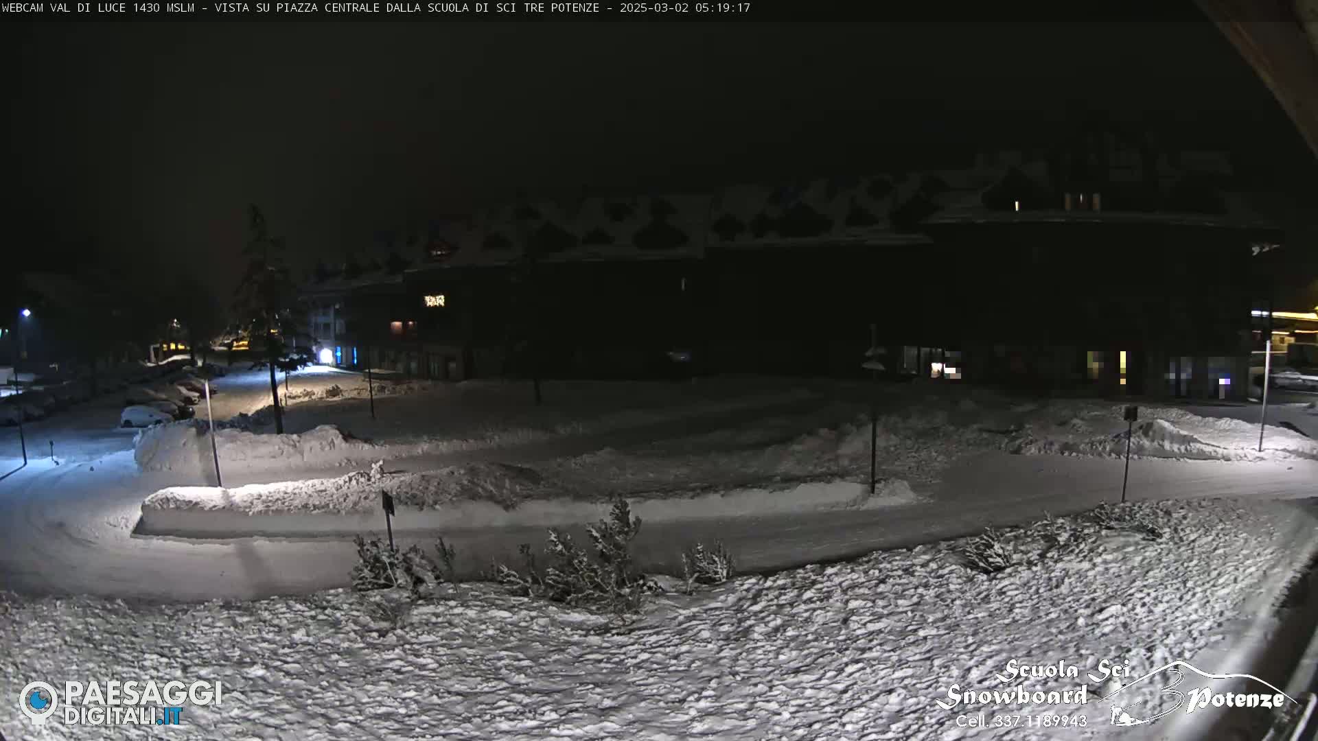 A snow-covered plaza at night, illuminated by streetlights, with a building in the background.