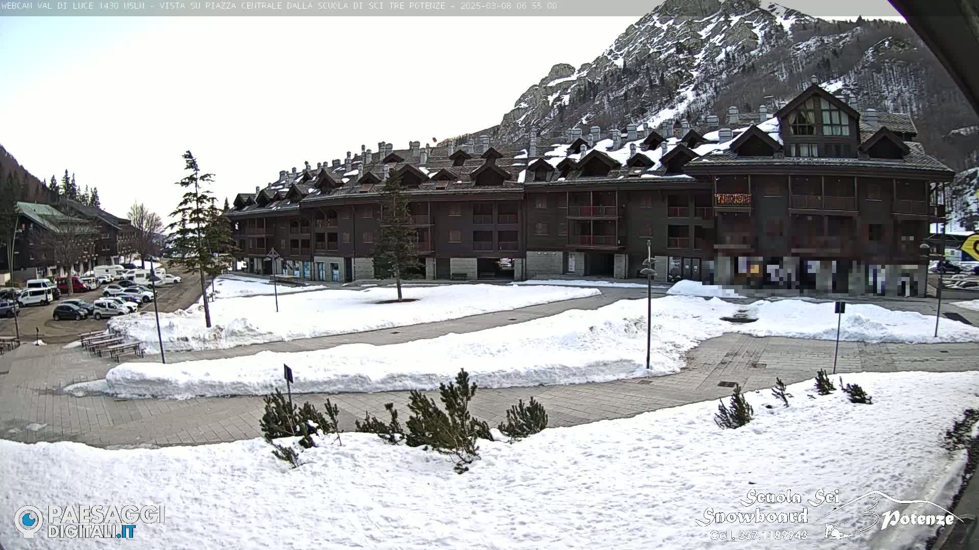 A snow-covered plaza with a multi-story building in the background, situated in a mountainous area.