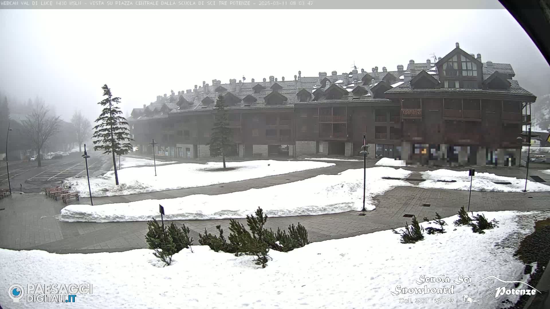 A snow-covered plaza sits in front of a multi-story building under foggy conditions.