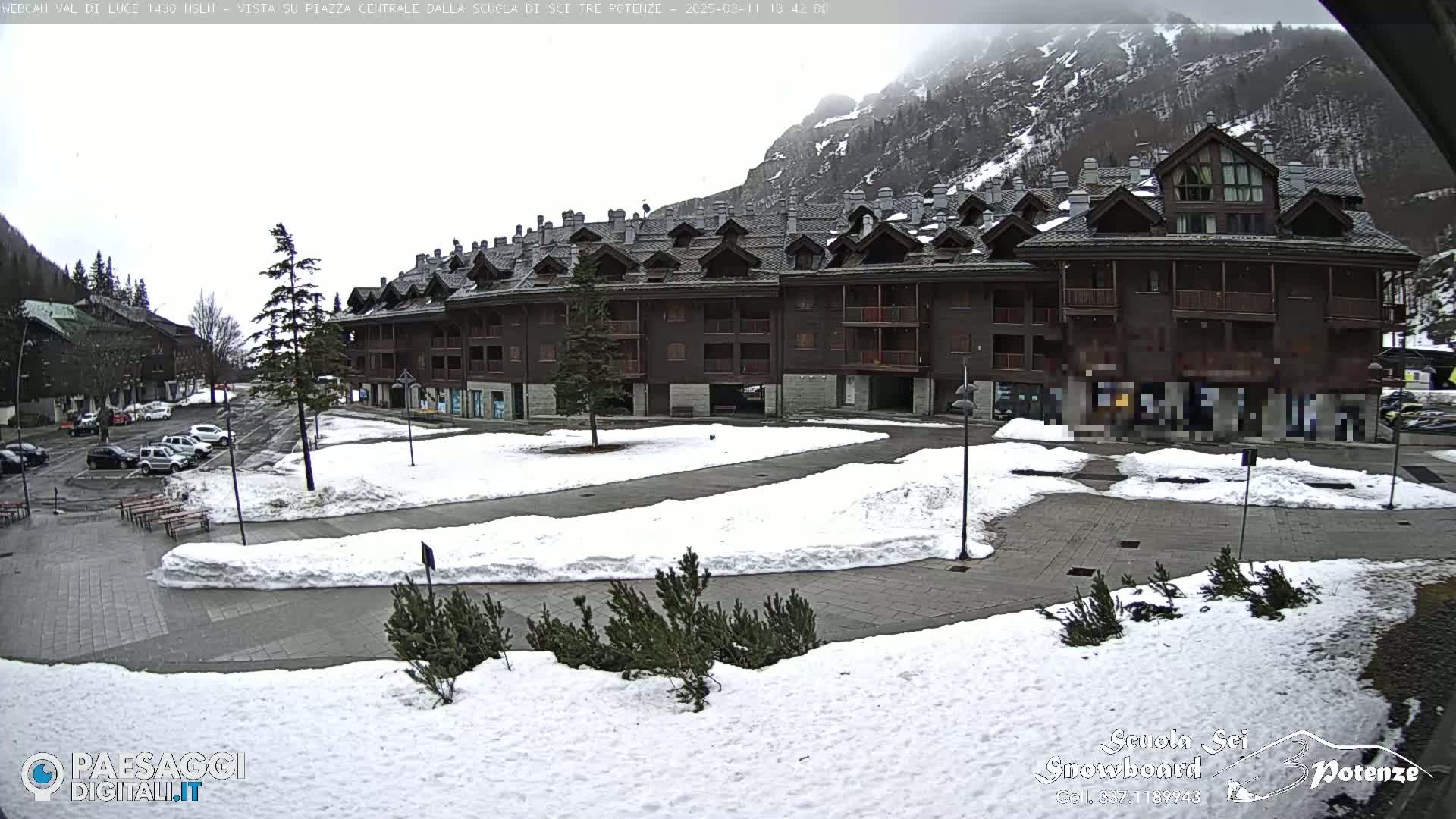 A snow-covered plaza with a multi-story building in the background, under an overcast sky.