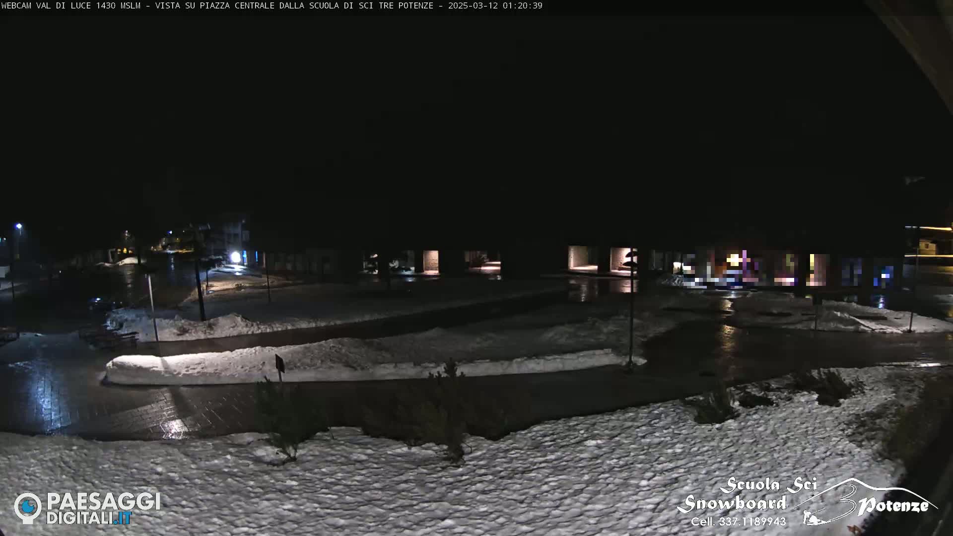 A nighttime view of a snow-covered plaza with patches of ice and dimly lit buildings surrounding it.