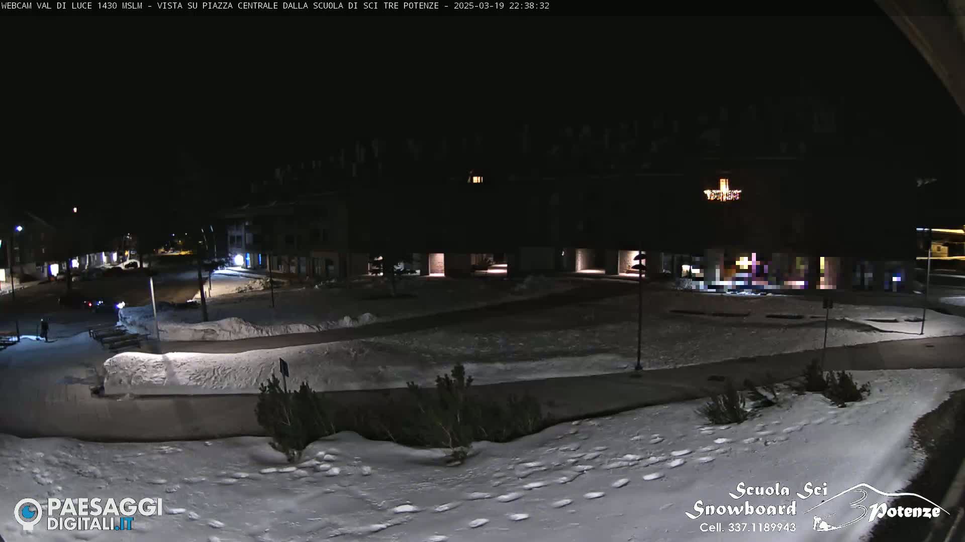 A snow-covered plaza at night, illuminated by building lights, with some footprints in the snow.