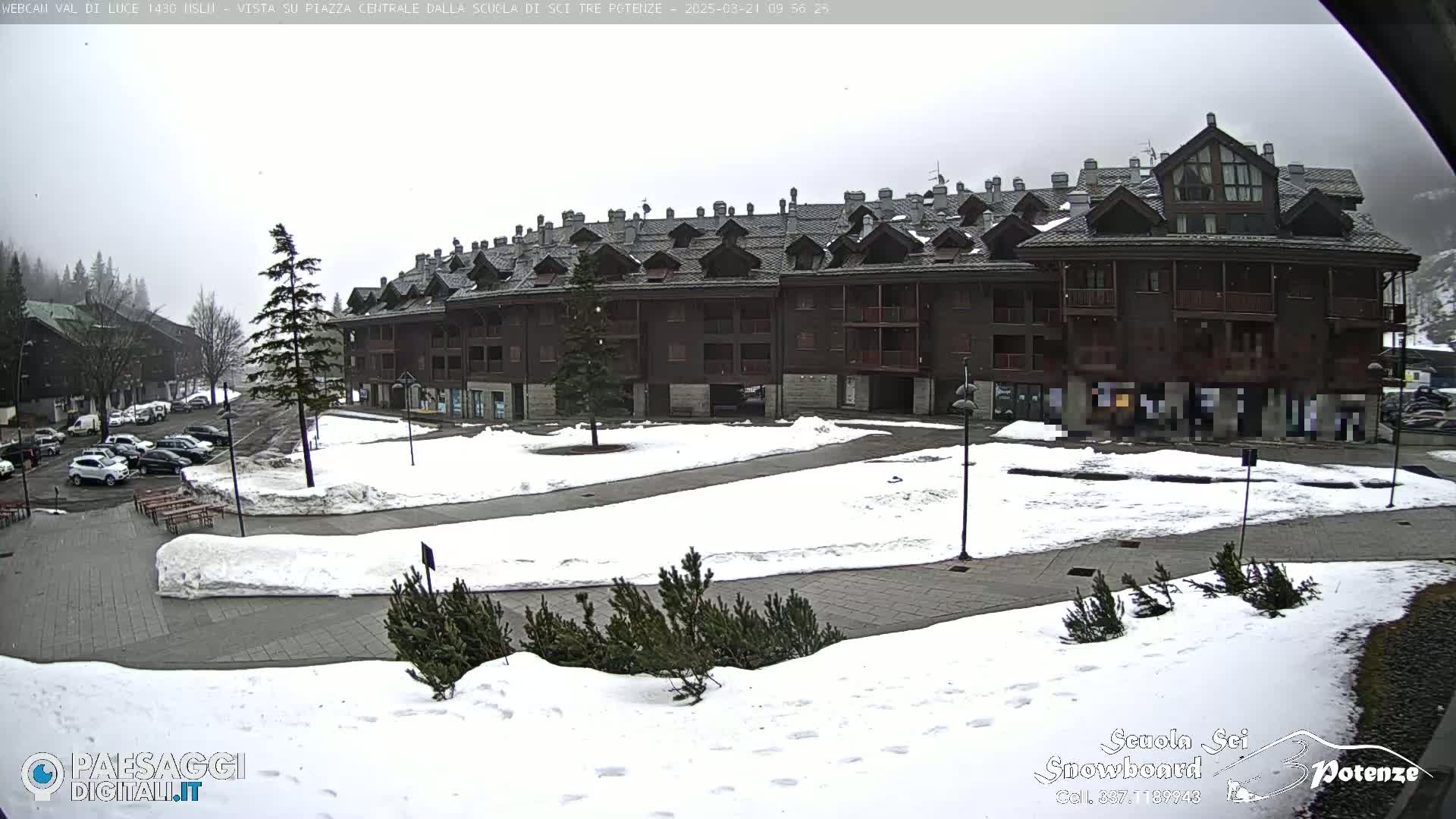 A snow-covered plaza sits in front of a large, multi-story brown building under an overcast sky.