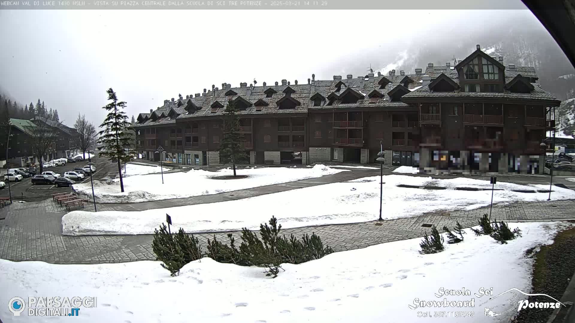 A snow-covered plaza in front of a multi-story brown building under an overcast sky.
