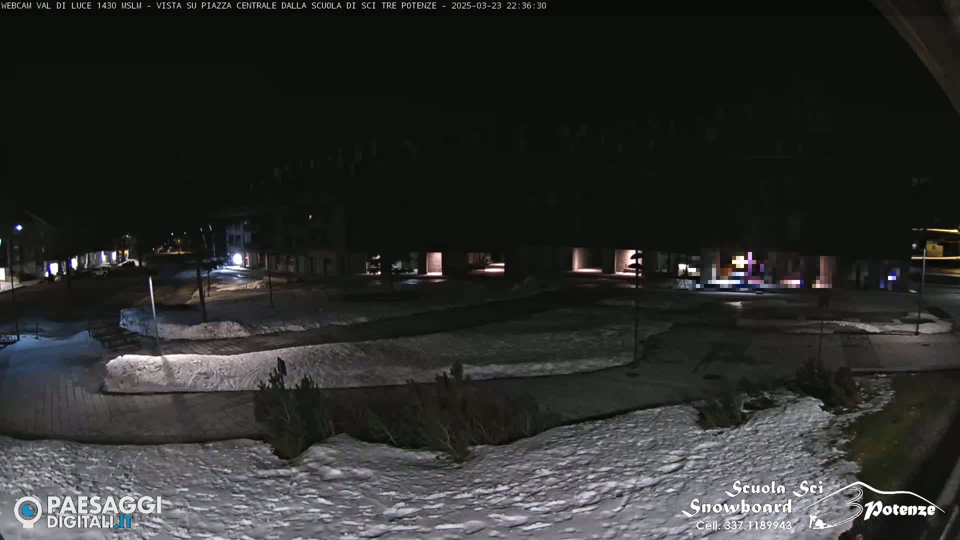 A snow-covered town square is dimly lit at night.