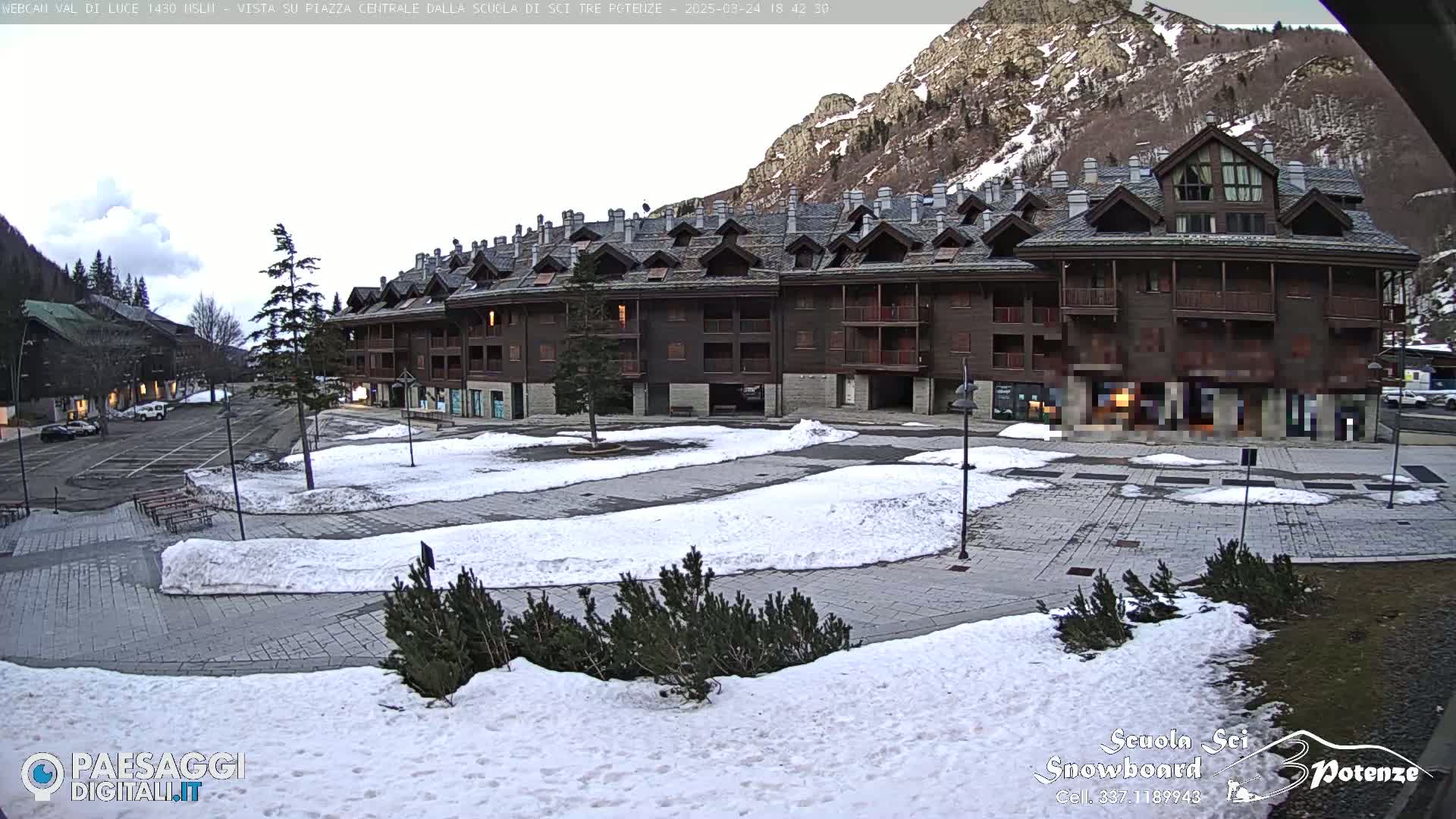 A snow-covered plaza sits in front of a multi-story building in a mountainous area.