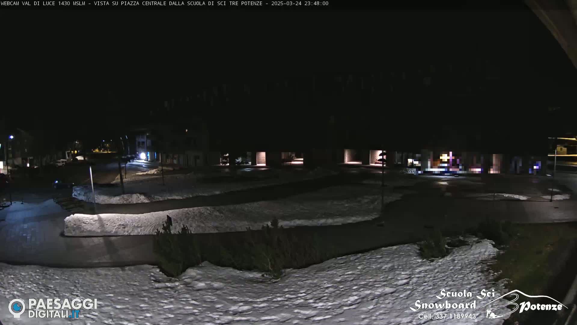 A nighttime view of a snow-covered plaza and surrounding buildings, illuminated by streetlights.