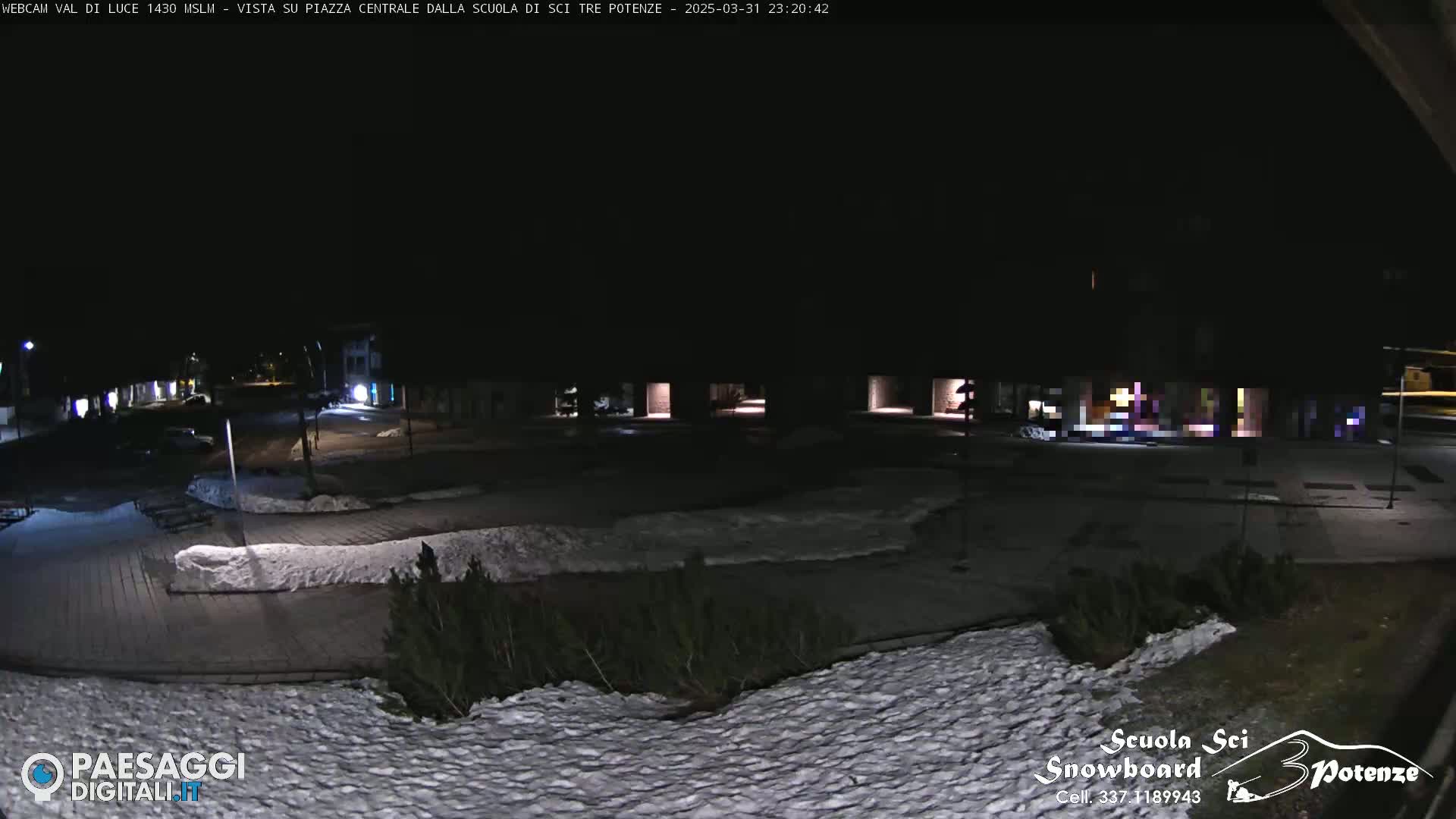 A nighttime view of a snow-covered plaza with sparsely lit buildings in the background.