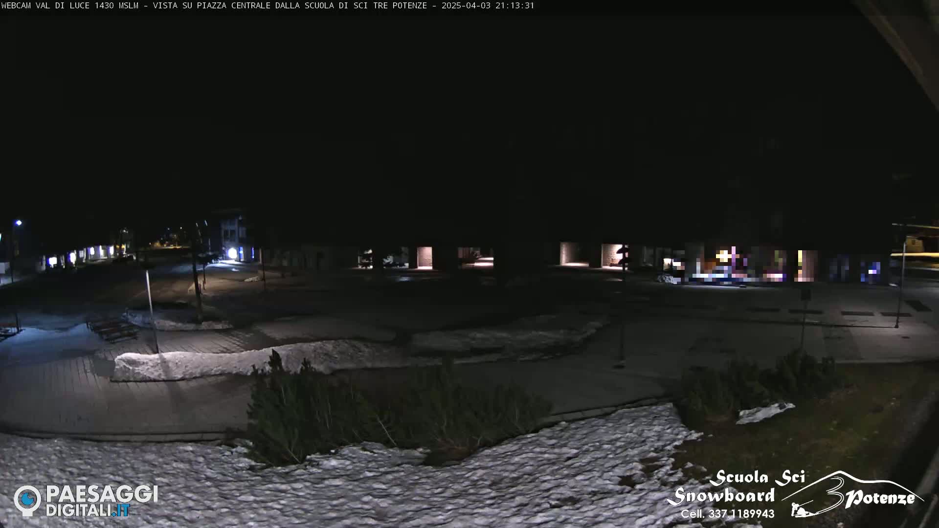 A nighttime view of a snow-covered plaza with low-level lighting and buildings in the background.