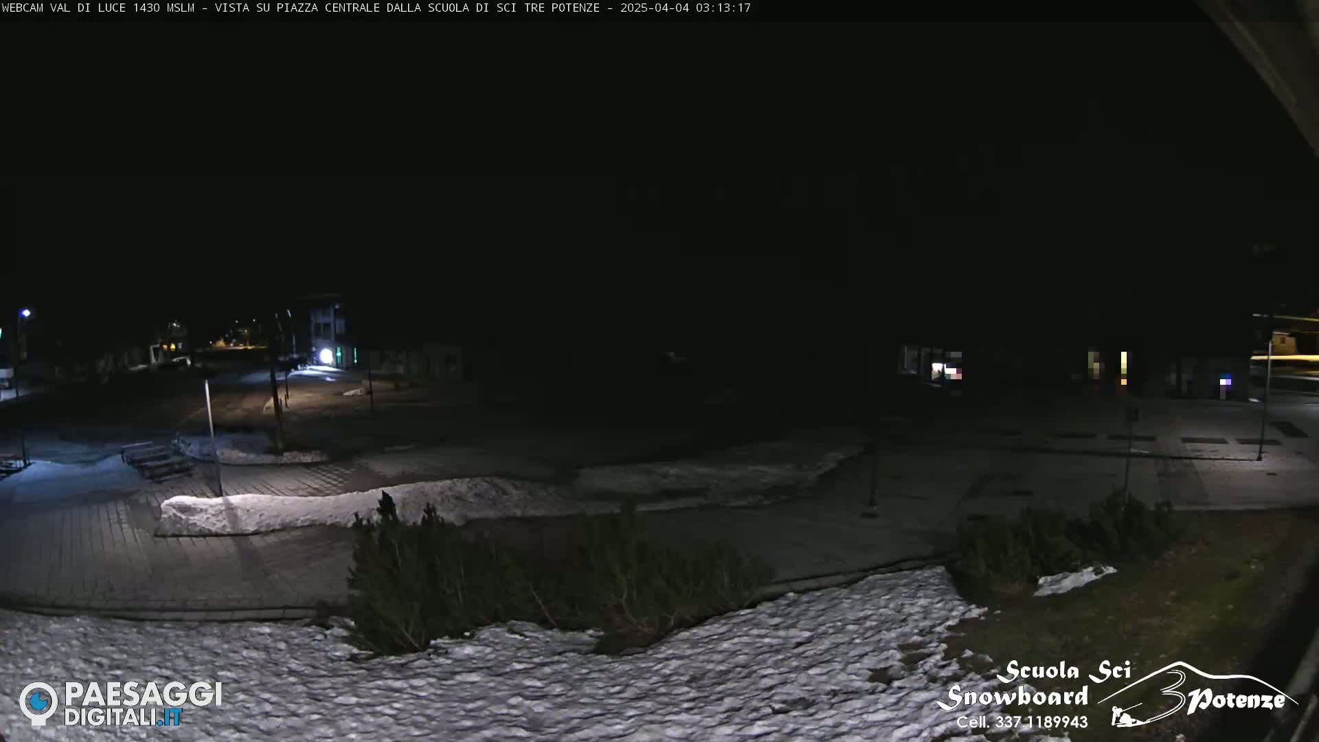 A nighttime view of a snow-dusted town square, dimly lit with a few lights visible in the distance.