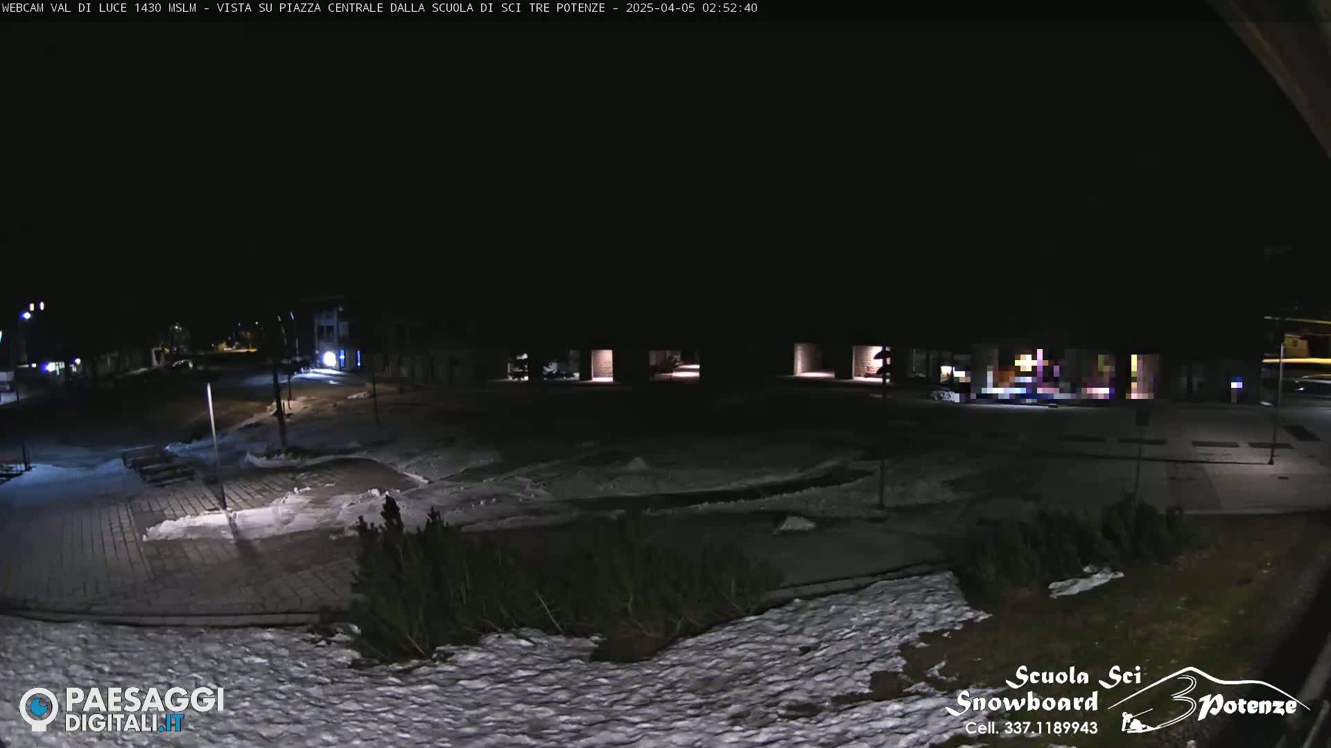 A snow-covered plaza is seen at night, illuminated by dim lights.