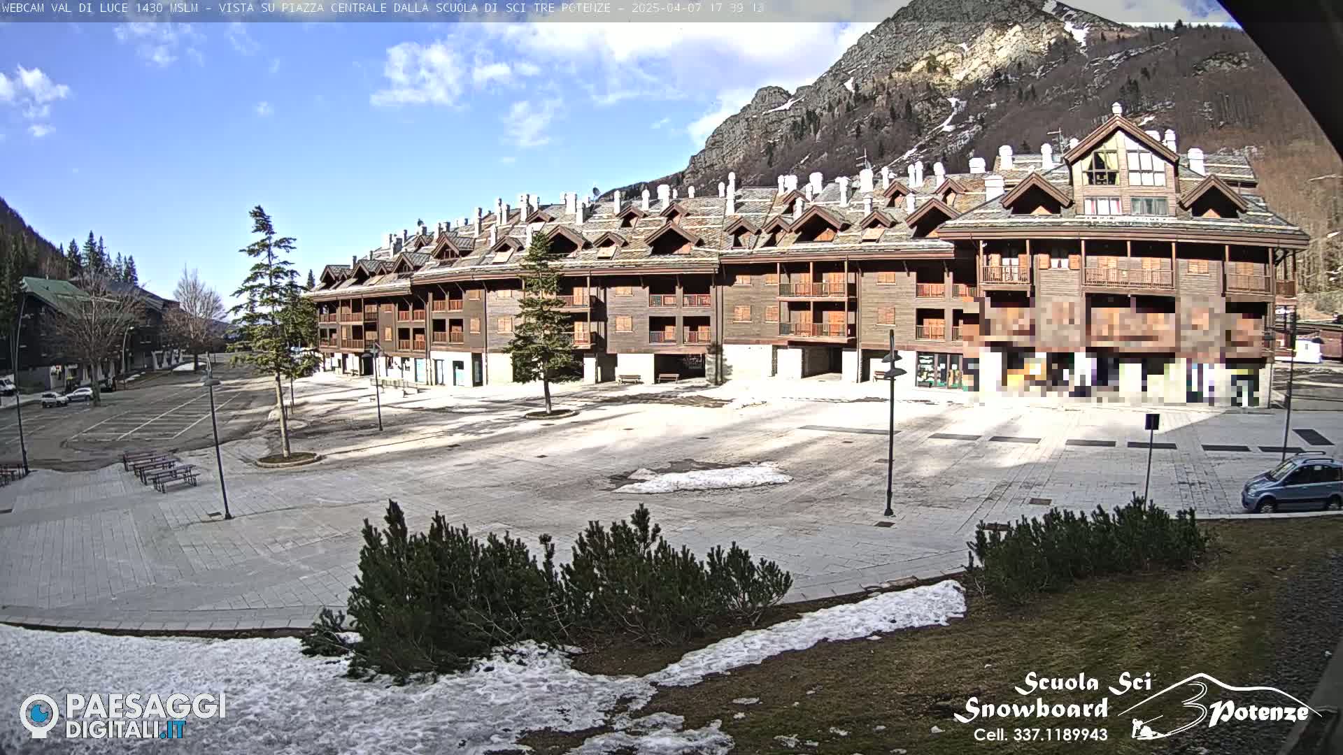 A large, wood-paneled apartment building overlooks a mostly empty plaza with patches of snow on the ground under a partly sunny sky.