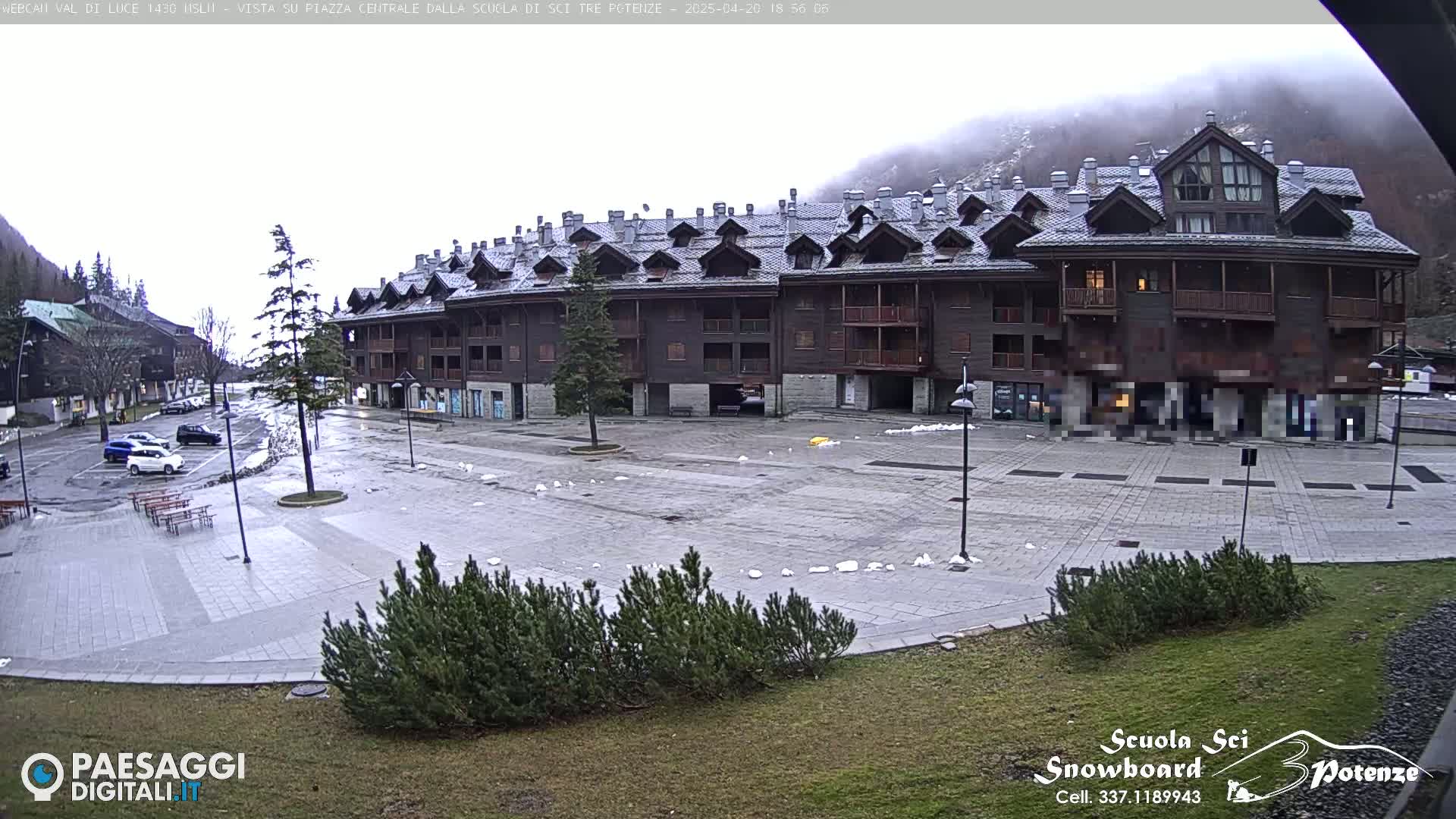 A large, multi-story, dark-wood building sits in a mostly empty paved square with small patches of snow on the ground under an overcast sky.