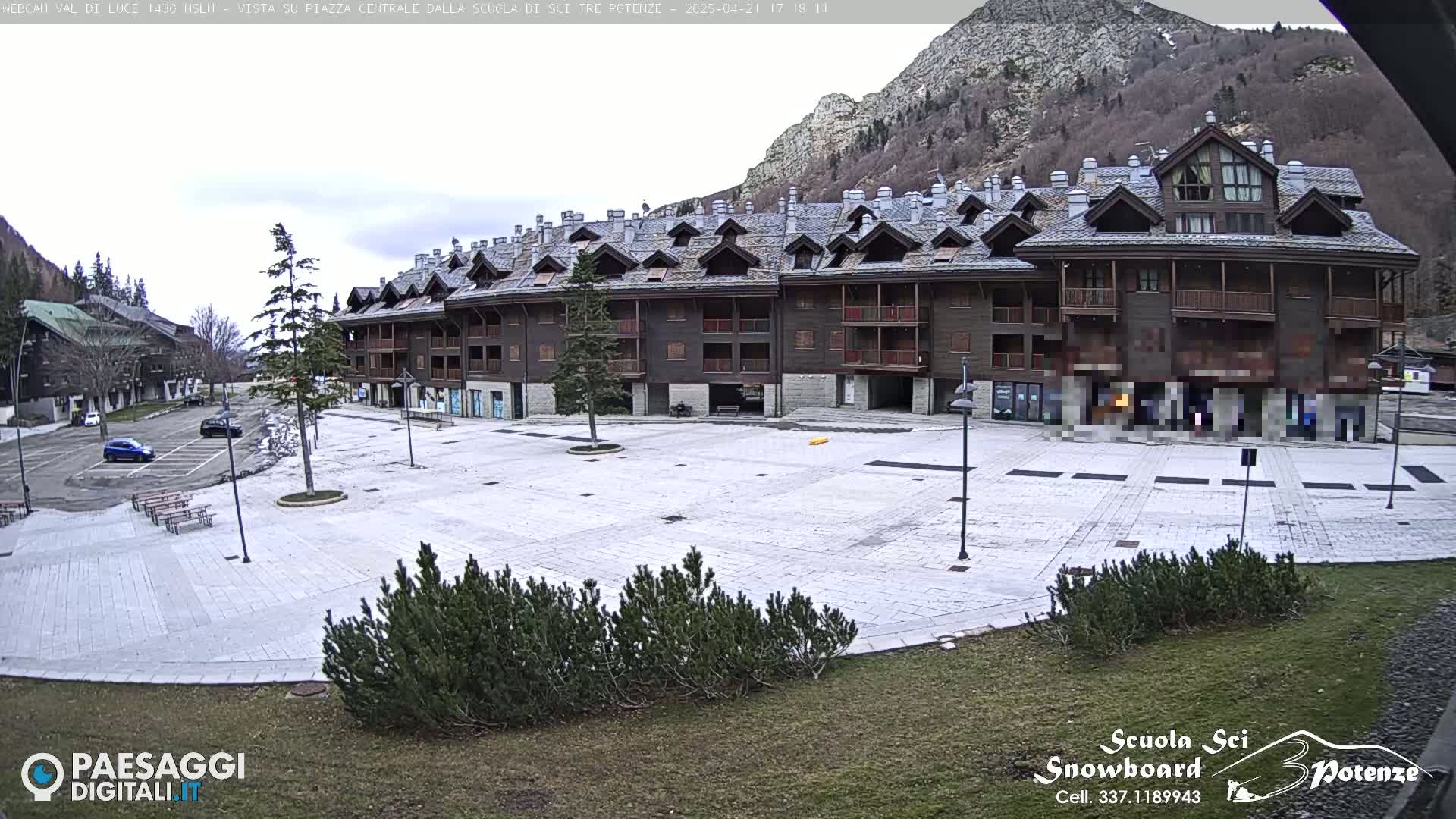 A large, empty plaza with a multi-story building behind it, situated in a mountainous area under an overcast sky.
