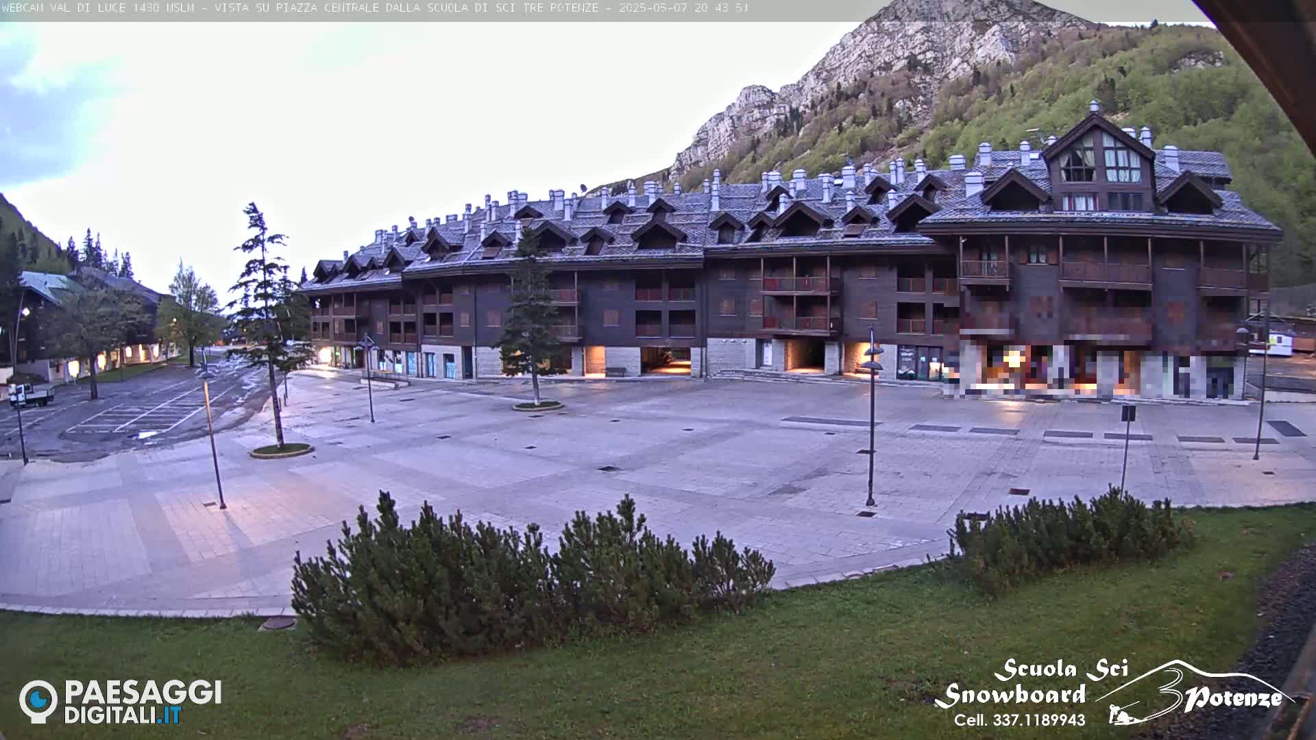 A large, multi-story building with a dark wood exterior and steeply pitched roofs sits in a plaza in the early evening, under a mostly clear sky with mountains in the background.