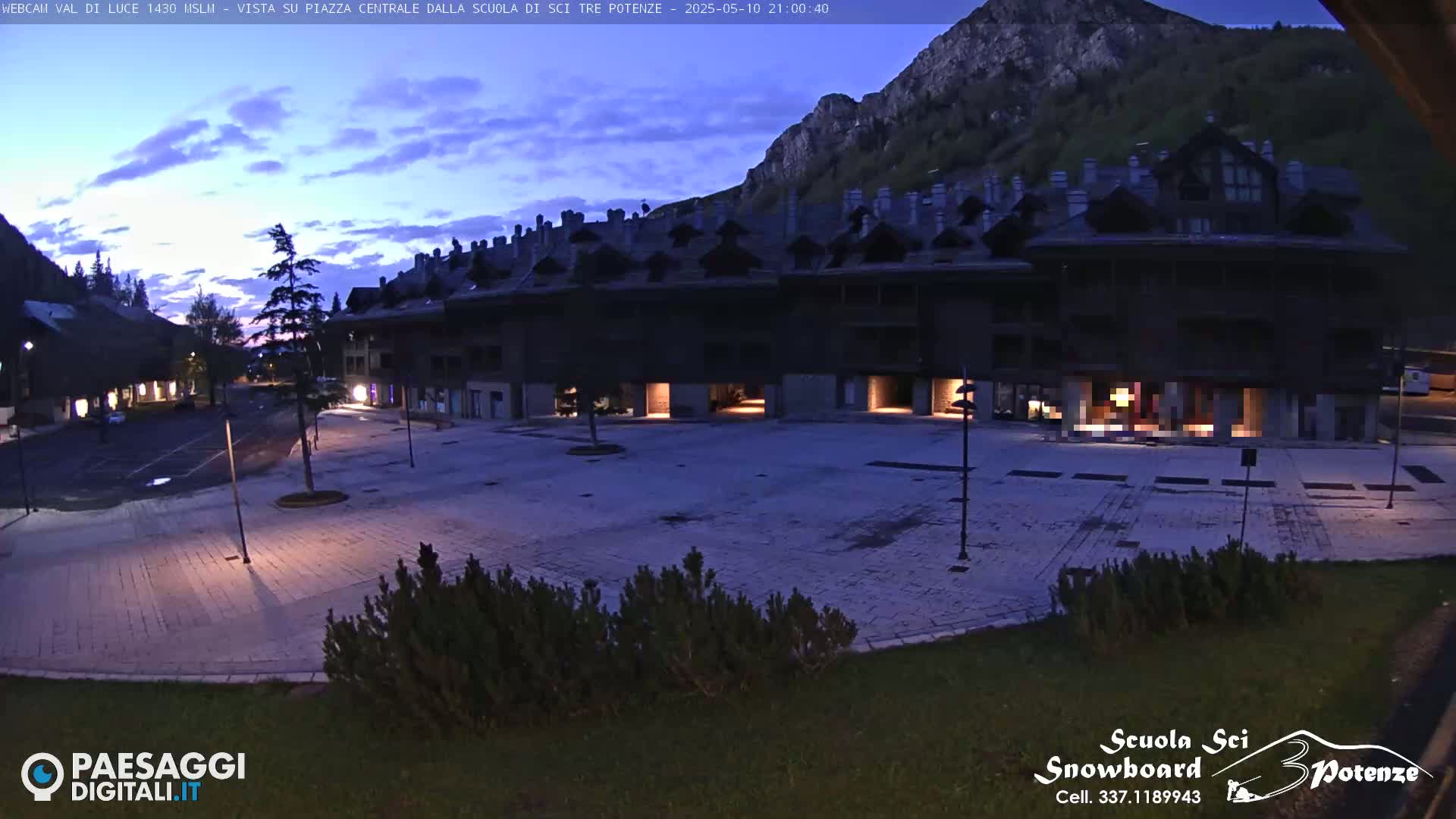 A mostly empty plaza is visible at twilight, with a large building behind it and a mountain in the background under a partly cloudy sky.