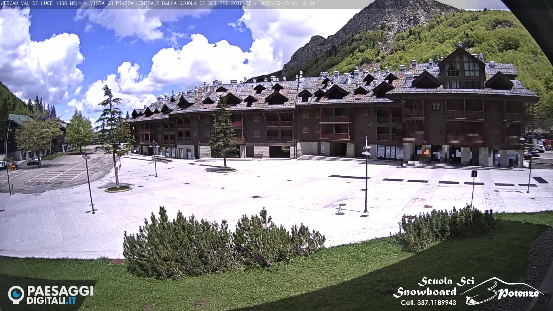 A large, empty plaza is situated in front of a multi-story, dark-brown building, all under a partly sunny sky.
