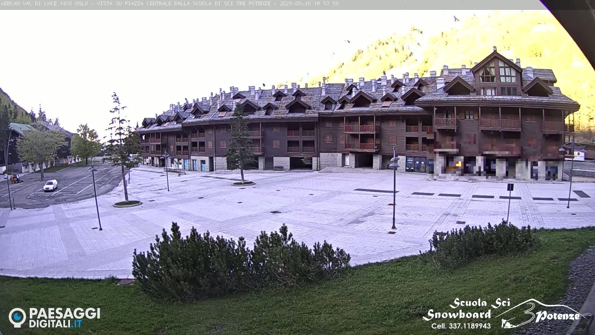 A mostly empty paved plaza sits in front of a large, multi-story wood-sided building, with a mountain in the background under a mostly clear sky.