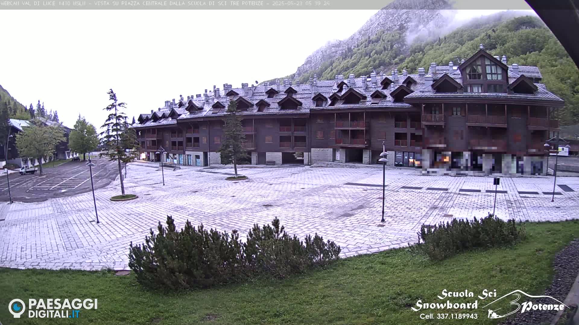 A large, multi-story wood-framed building sits in a stone plaza in front of a mountain shrouded in mist.