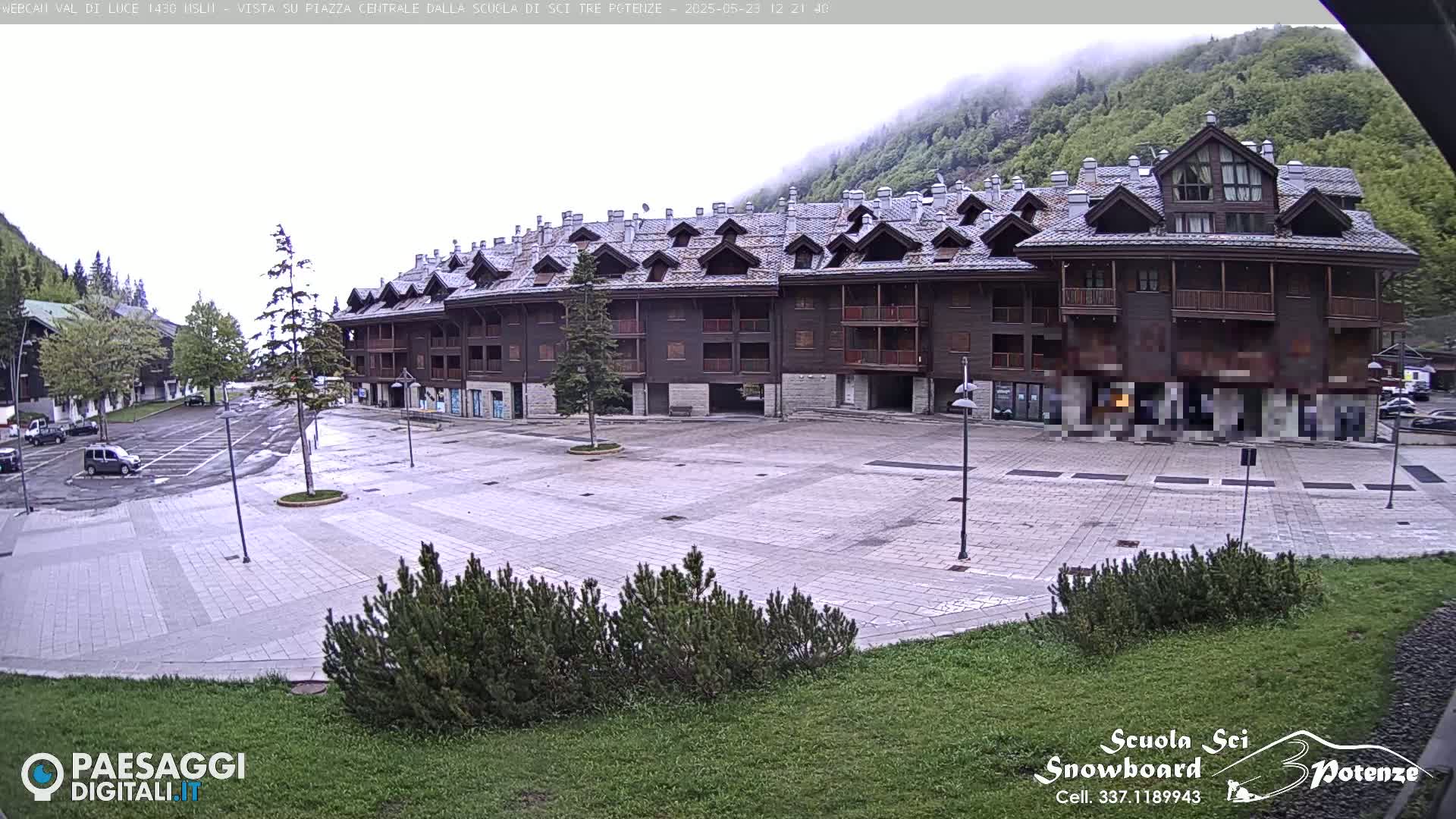 A large, empty plaza is situated in front of a multi-story brown building, with a mountain shrouded in fog in the background.