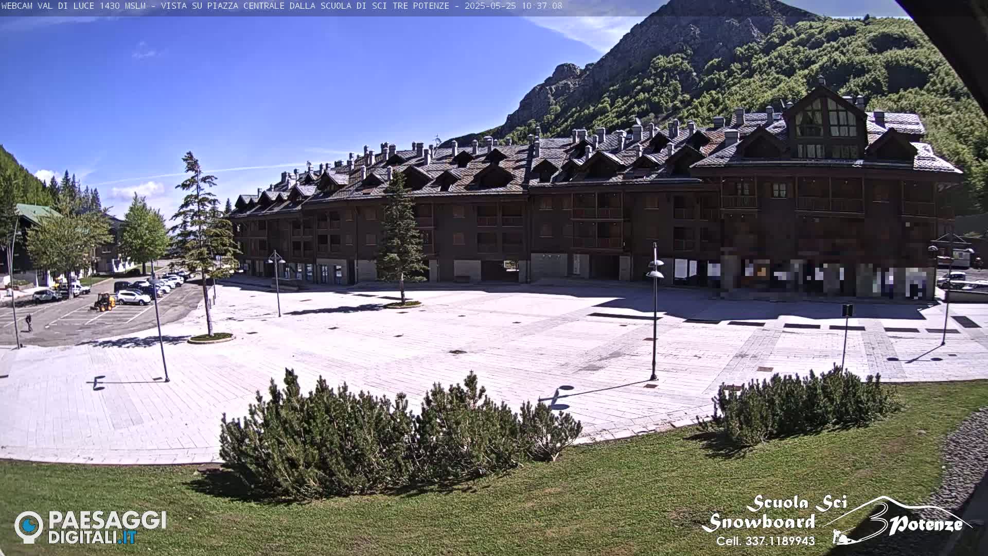A large, paved plaza sits in front of a multi-story building, with a mountain and clear blue sky in the background.