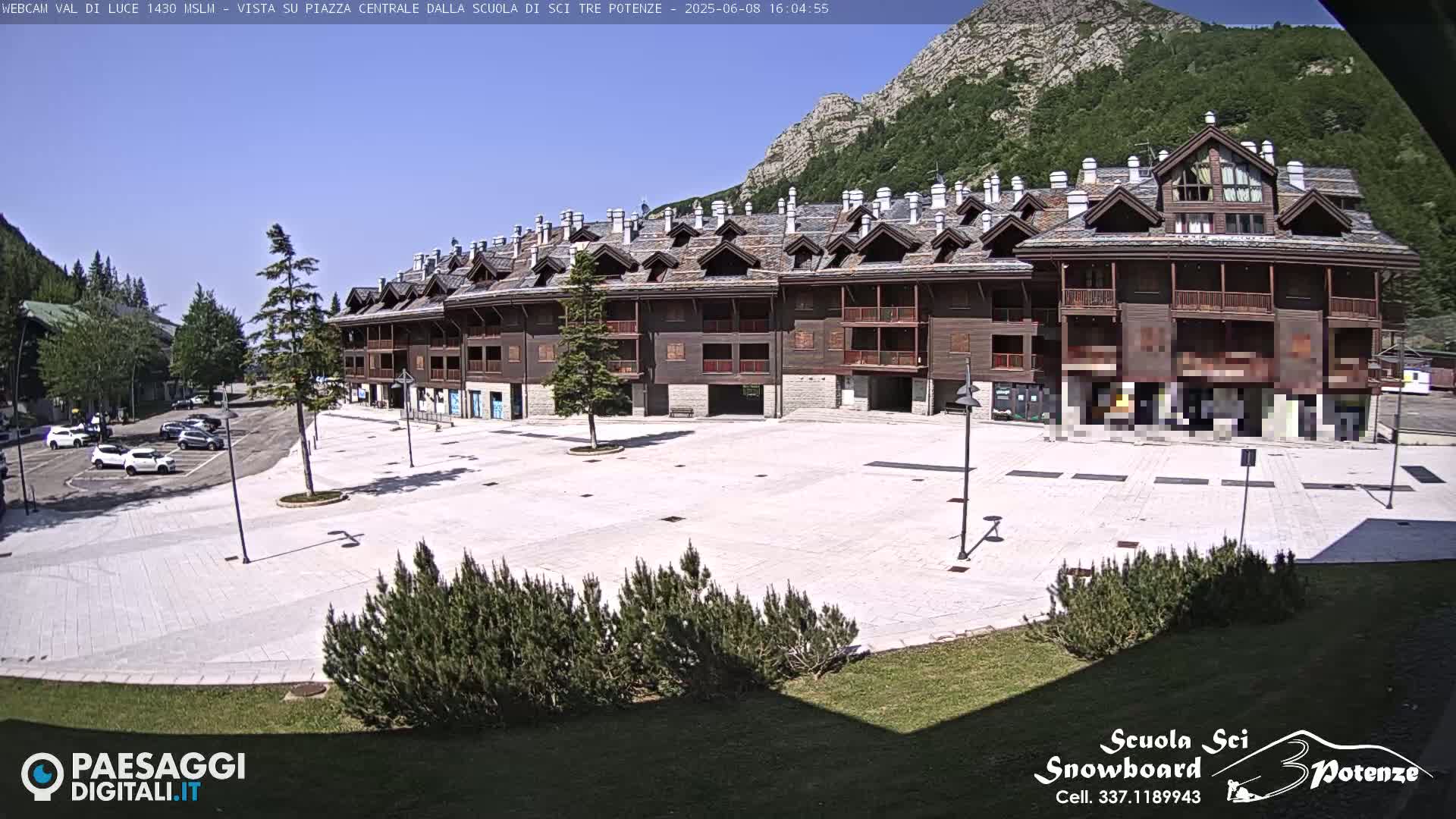 A large, empty plaza in front of a multi-story wood-sided building, with mountains and a clear sunny sky in the background.
