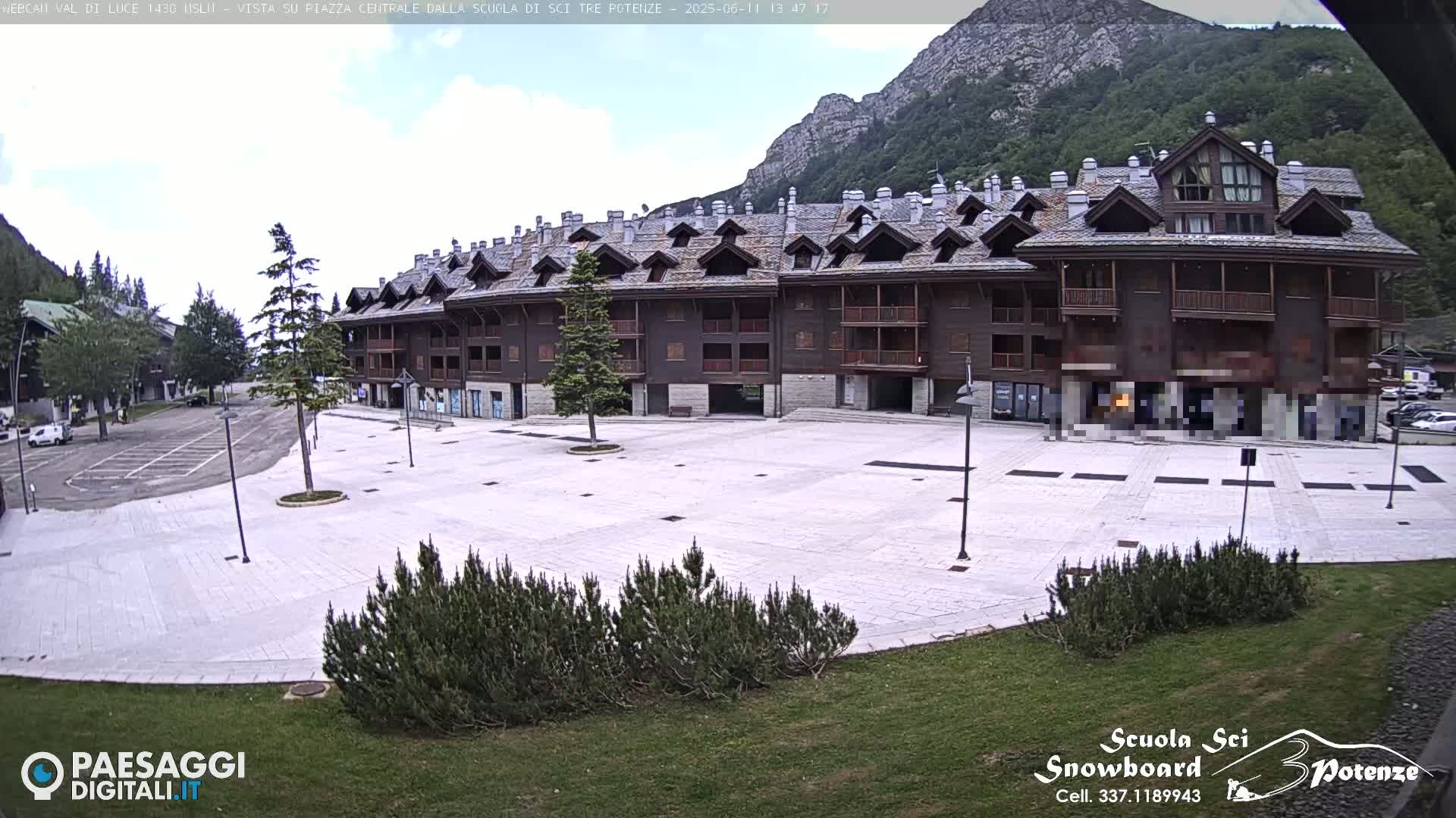 A large, empty paved plaza sits in front of a multi-story brown building, with mountains and partly cloudy skies in the background.