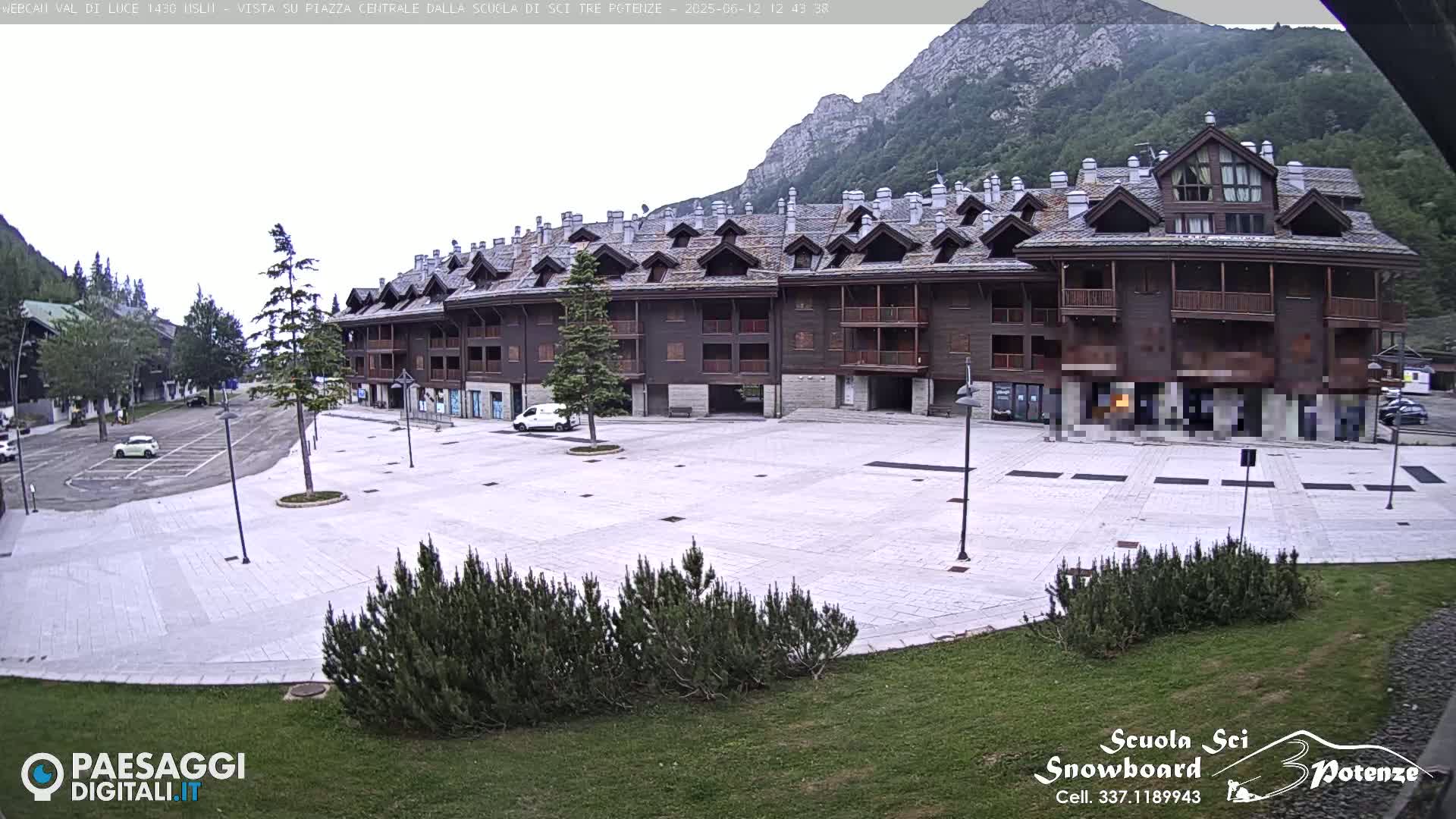 A large, empty paved square sits in front of a multi-story brown building, with mountains in the background under an overcast sky.