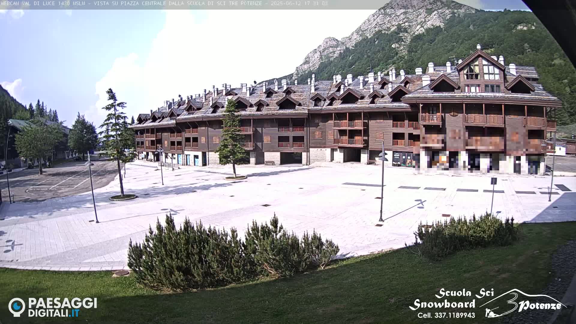 A large, empty plaza paved in light-colored stone sits in front of a multi-story brown wood building, with mountains and a partly cloudy sky in the background.