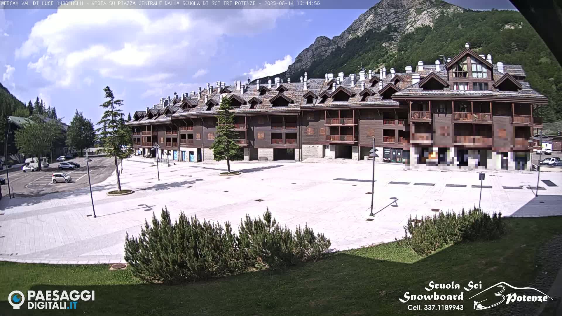 A large, light-colored plaza sits in front of a multi-story building with brown wooden siding, under a partly cloudy sky, with mountains visible in the background.