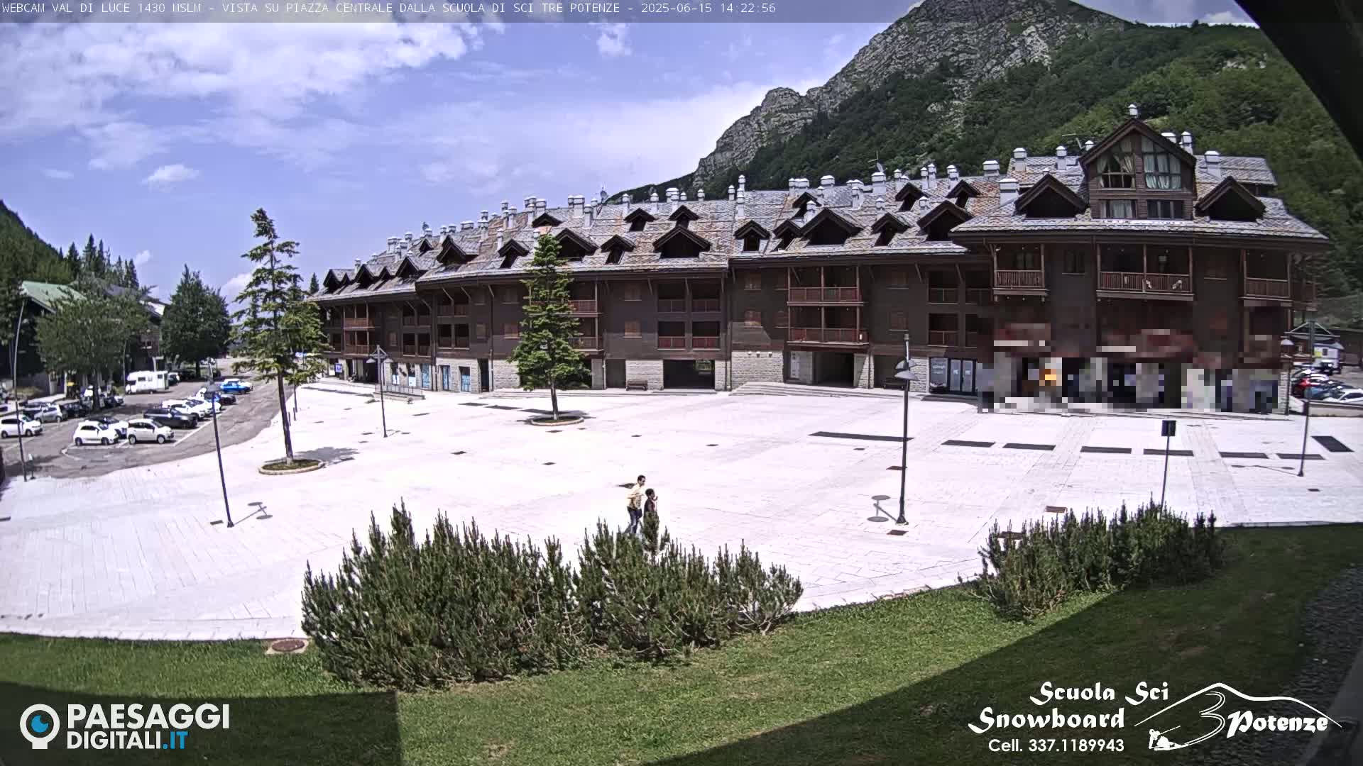 A large, light-colored plaza sits in front of a multi-story, brown wood-and-stone building, with mountains in the background under a partly cloudy sky.