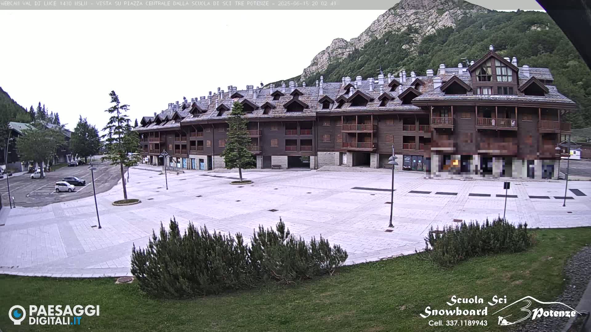 A large, light-colored plaza sits in front of a multi-story brown building in a mountainous area under an overcast sky.
