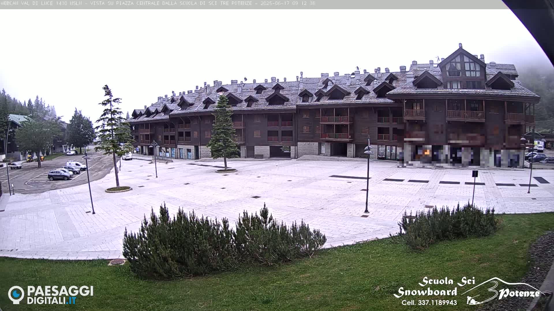 A large, dark-brown multi-story building overlooks a mostly empty paved square on an overcast day.