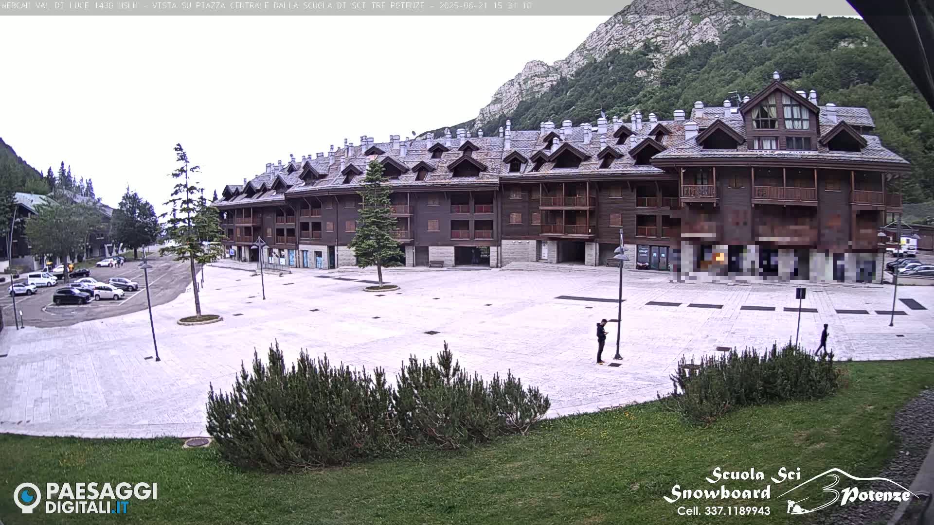 A large, wood-paneled building sits in a plaza overlooking a parking lot and mountains under an overcast sky.