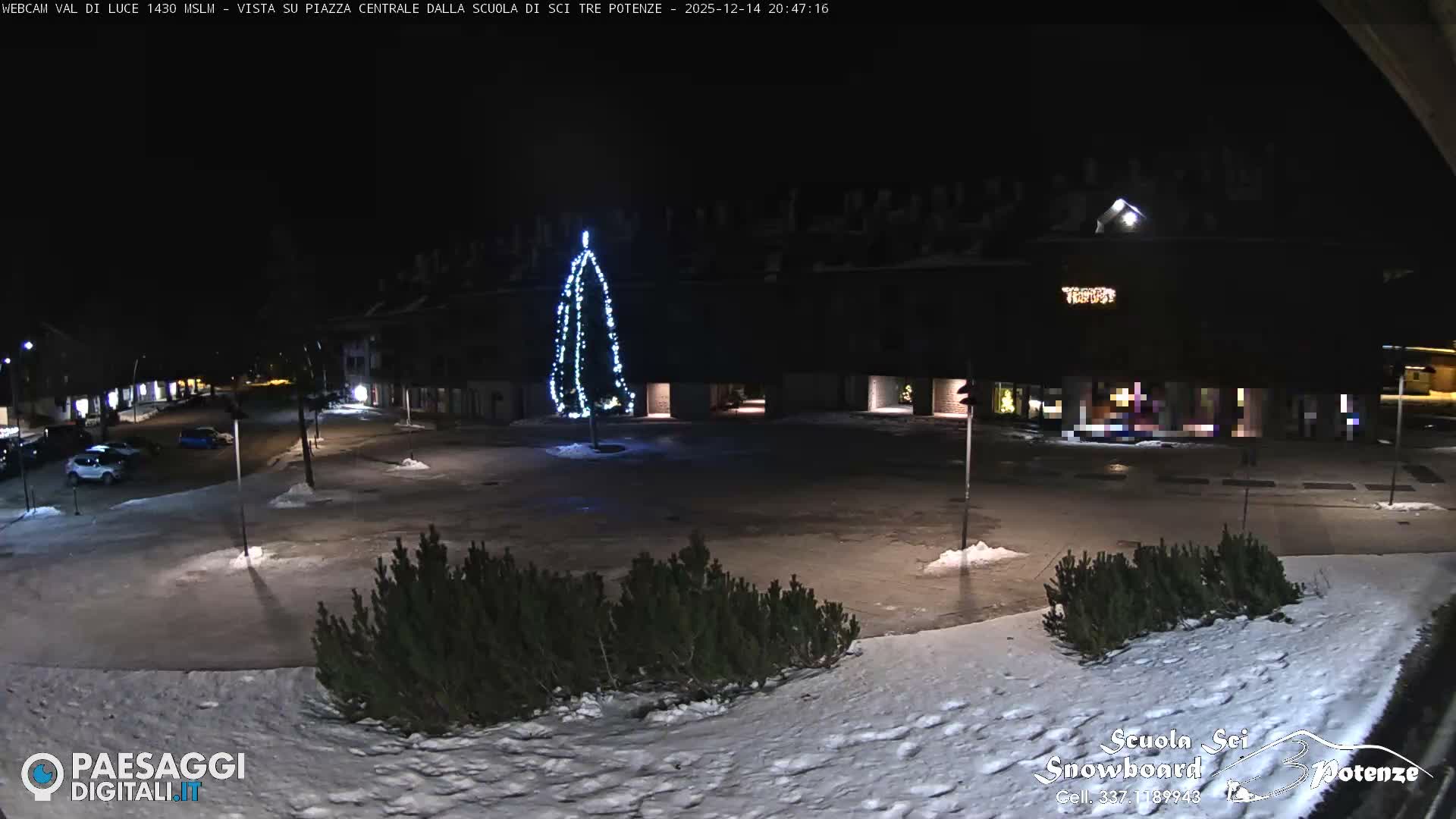 A snow-covered alpine village with a large lodge and several vehicles on partially cleared roads is enveloped in thick fog, severely limiting visibility.