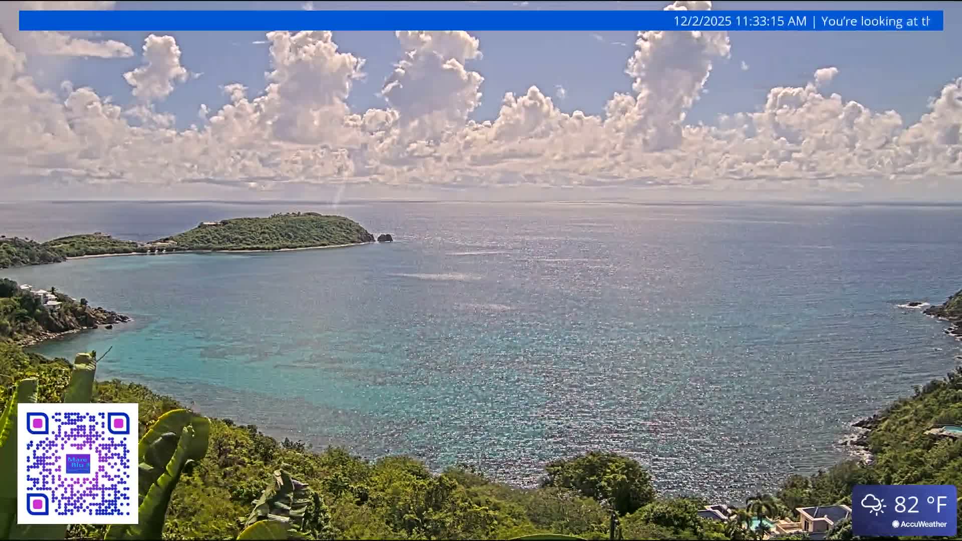 A sunny day with scattered white clouds overlooks a vibrant tropical bay, featuring clear turquoise waters, lush green islands, and distant hills.