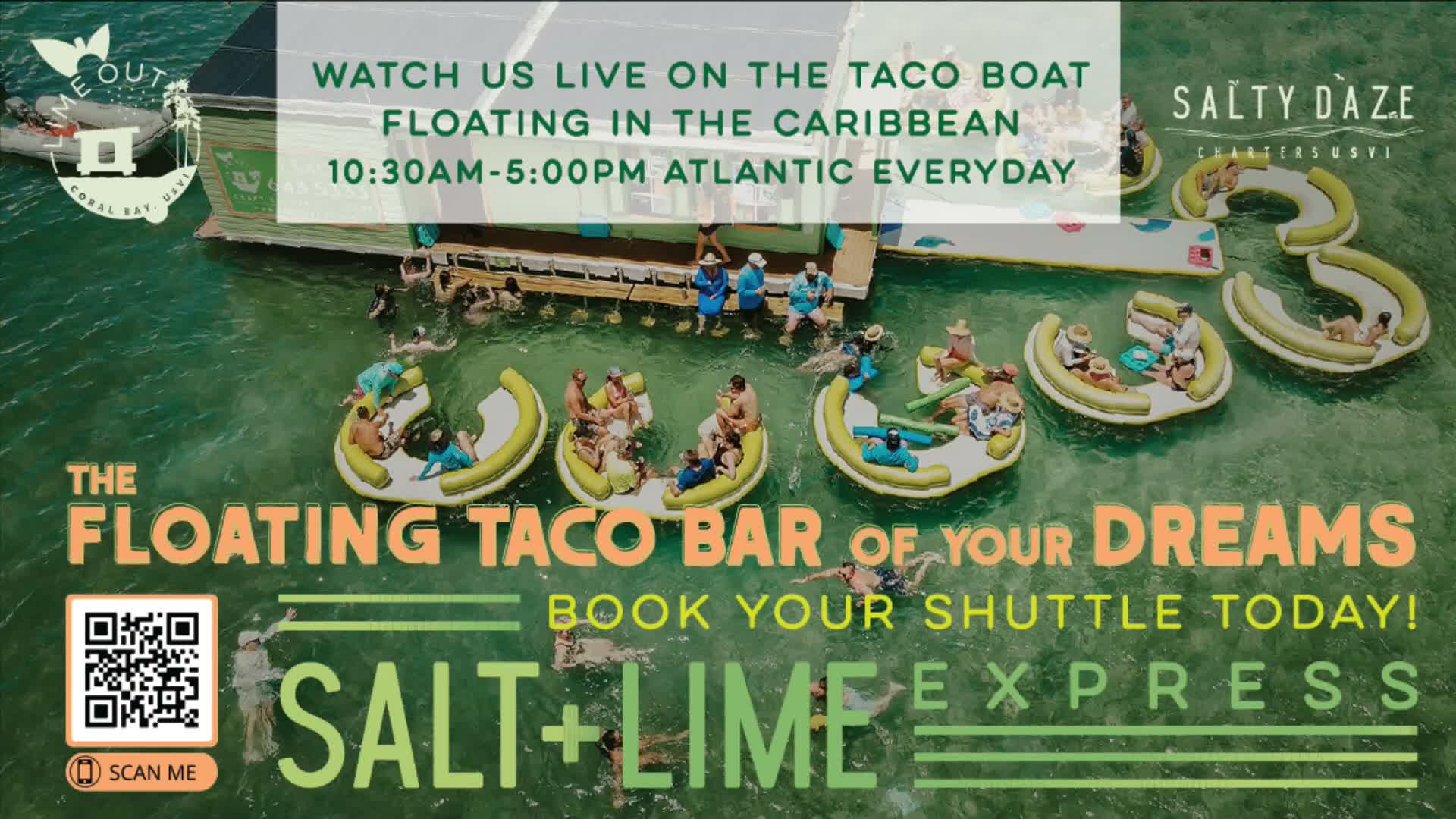 On a bright, sunny day, numerous people relax on and around a light green floating bar and yellow inflatables in the calm, clear waters of a tropical bay, with lush green hills and distant boats under a clear sky, as viewed from behind a person holding a pink tumbler.